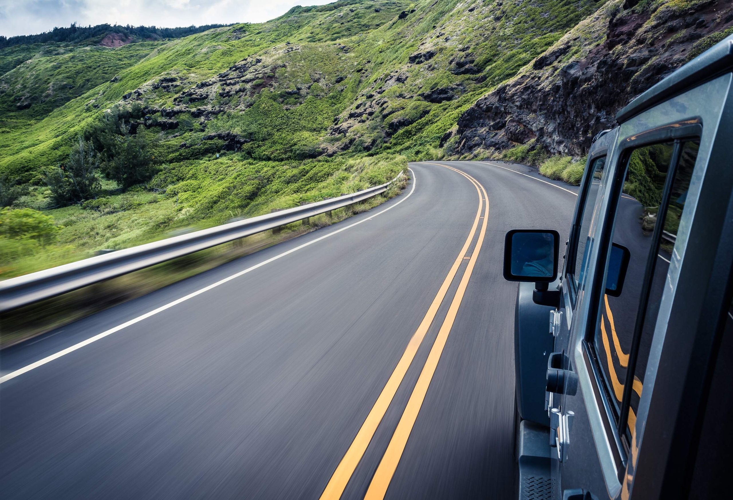 A car speeding down along an asphalt road that runs along the hillsides.