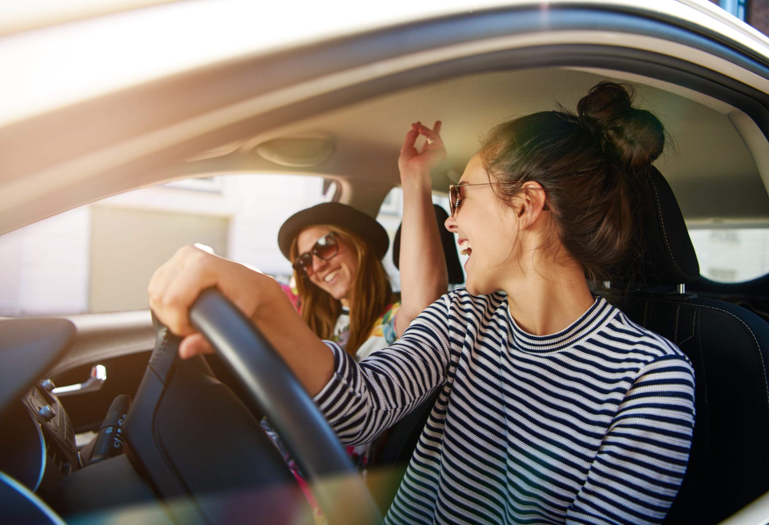 Female driver in striped shirt glances at her passenger inside the car while laughing.