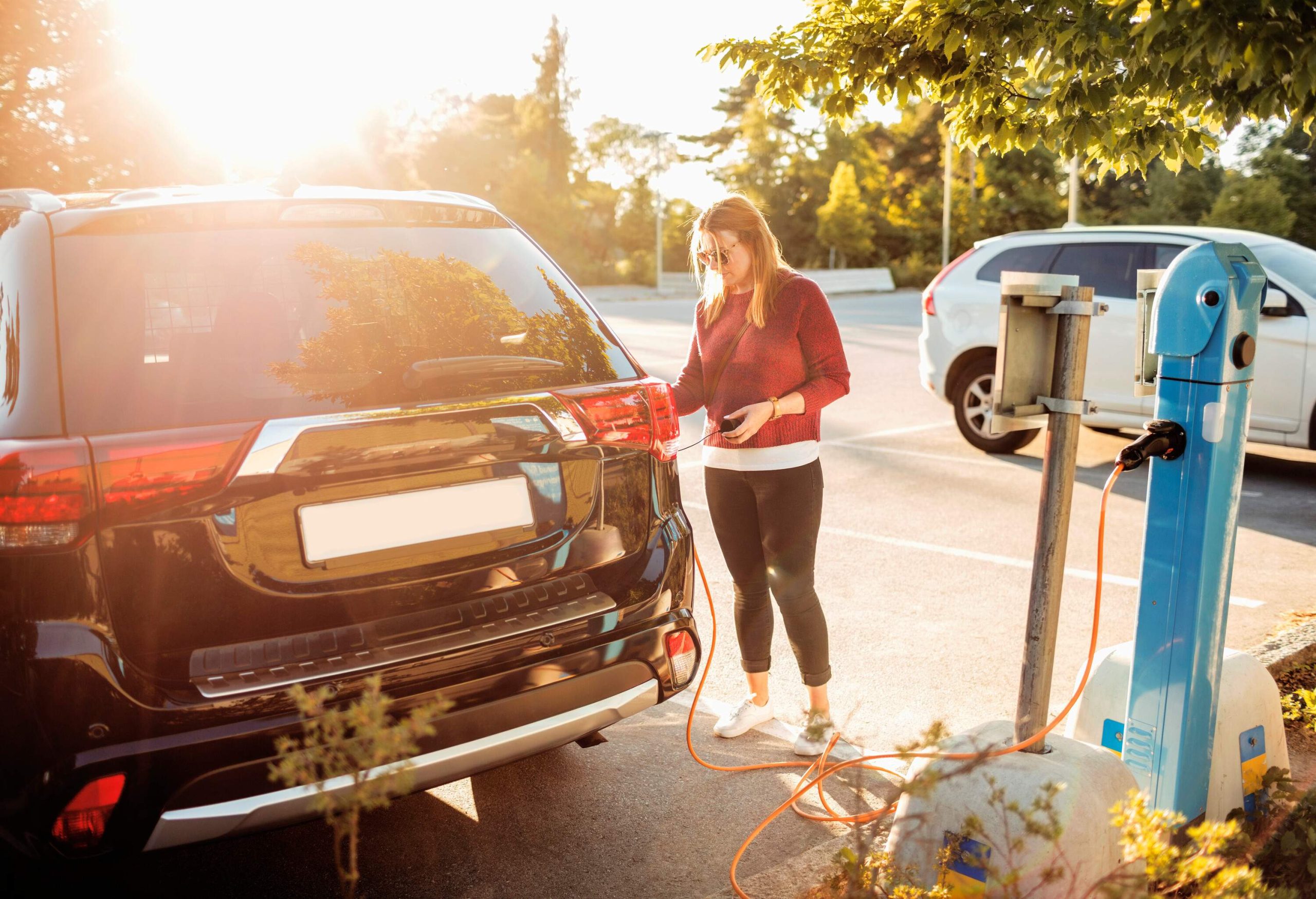 A woman charges an electric car with a cable in a charging station parking lot.