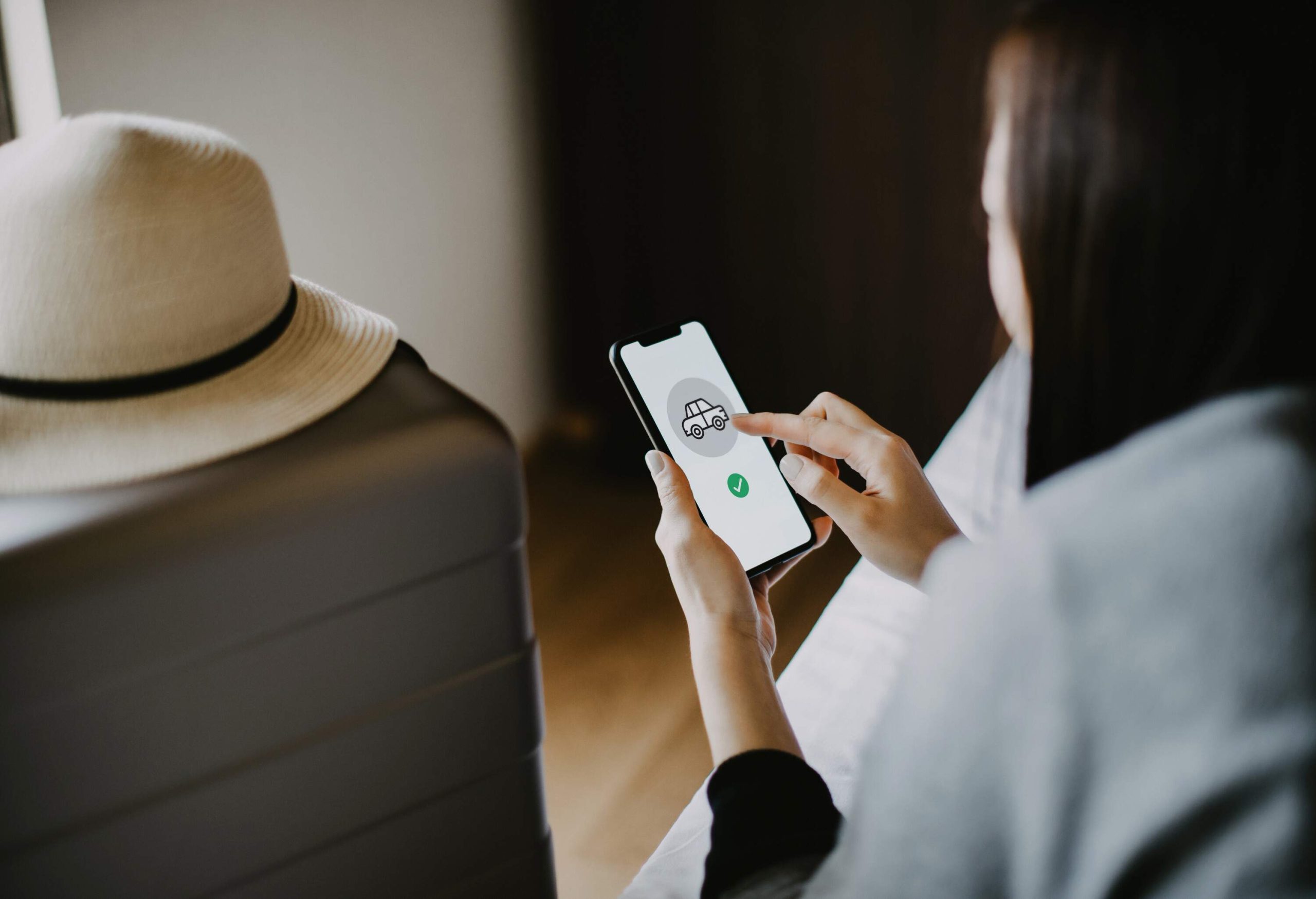 A woman booking a car using her smartphone sitting on her hotel bed.