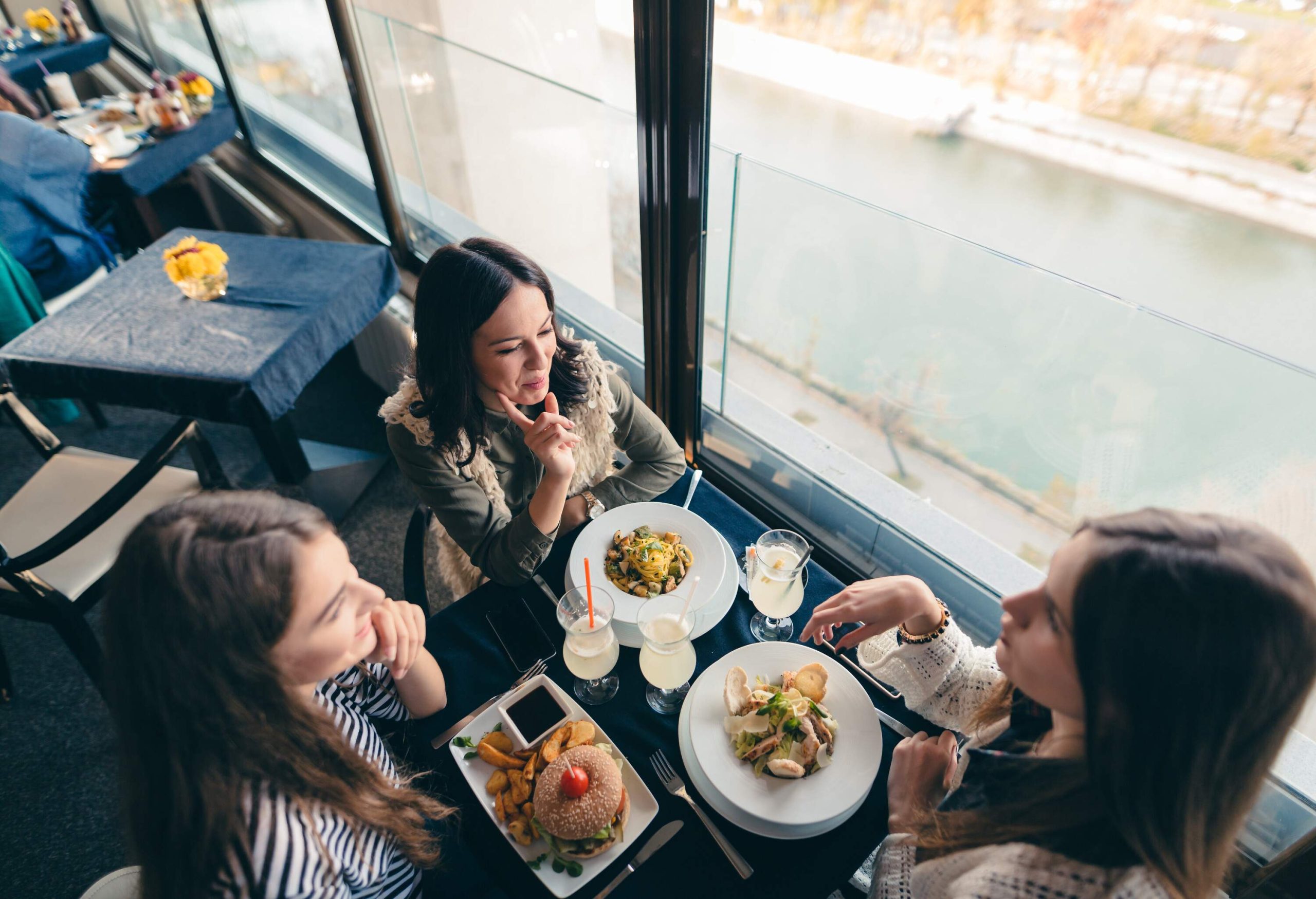 Three women seated at a restaurant table by the window with scrumptious dishes before them.