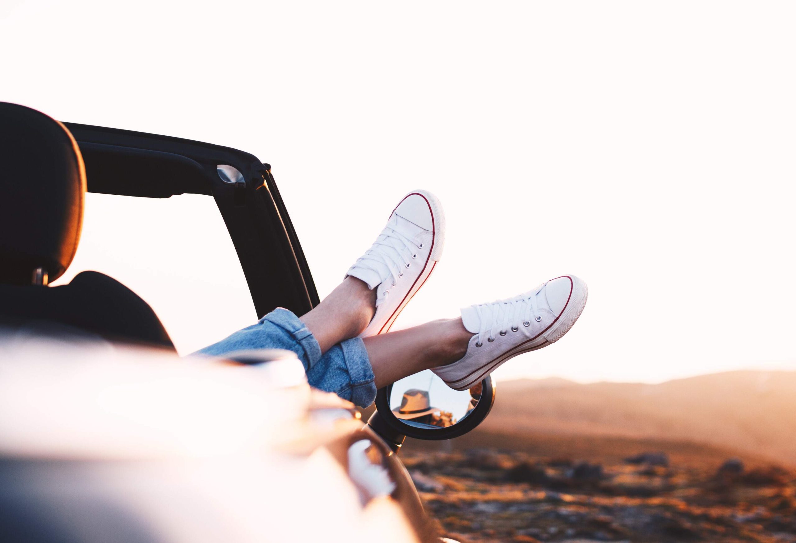 A person's feet in white sneakers, hanging outside the convertible cars.