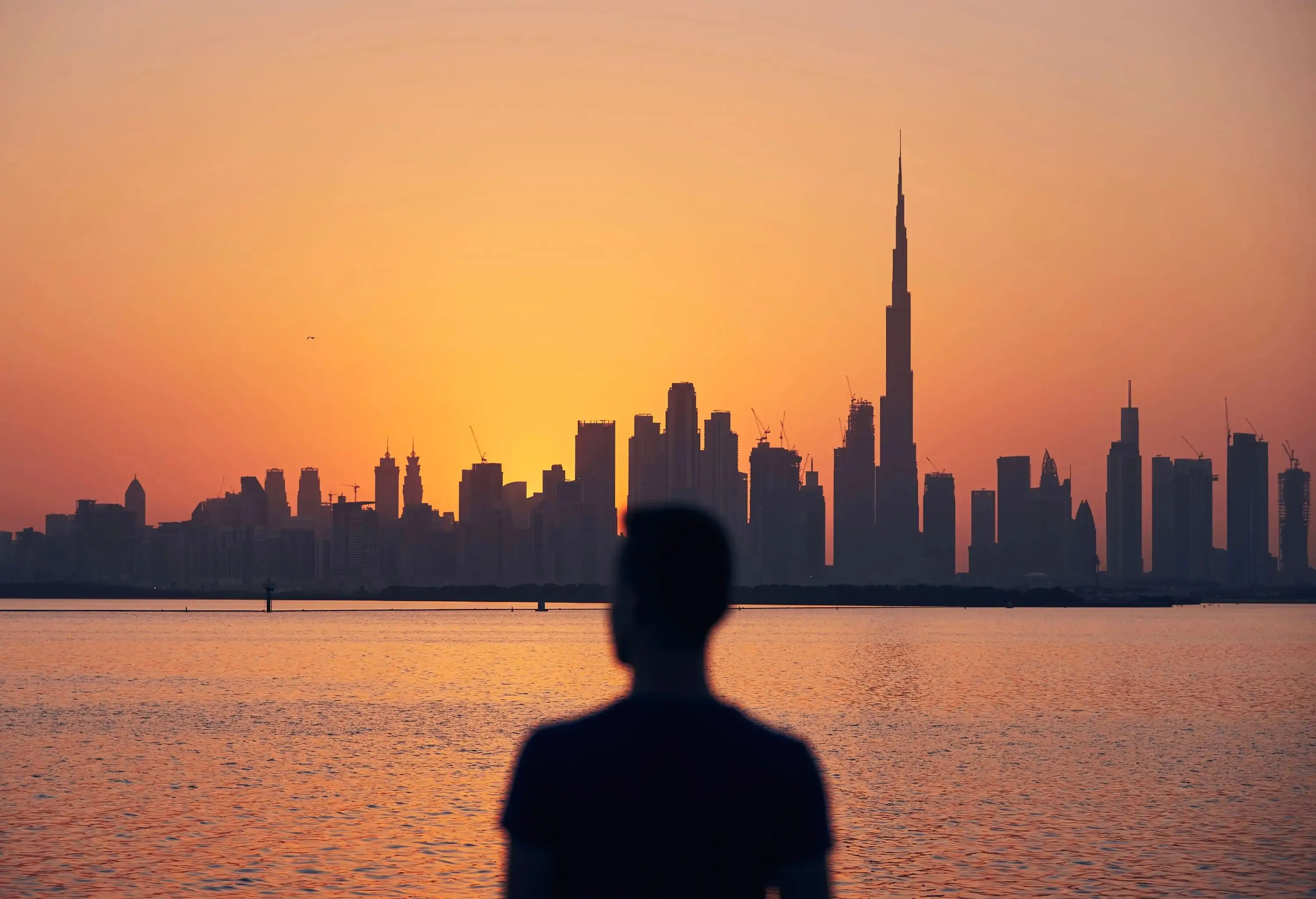 Silhouette of lonely man looking at cityscape at beautiful dusk. Urban skyline with tallest skyscraper Burj Khalifa, Dubai, United Arab Emirates.