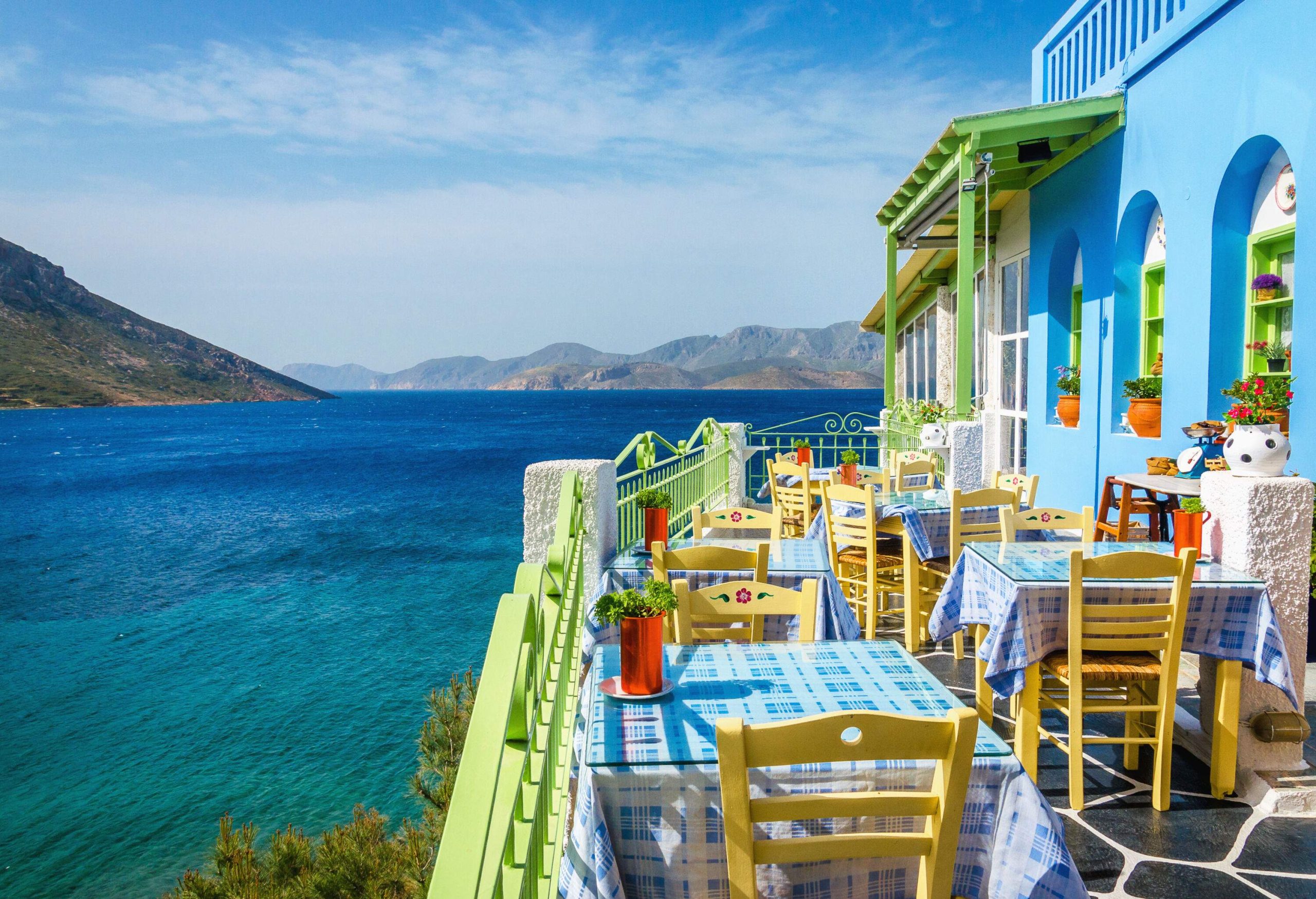 A sky blue restaurant with an outdoor dining area on a balcony with sweeping views of the sea.