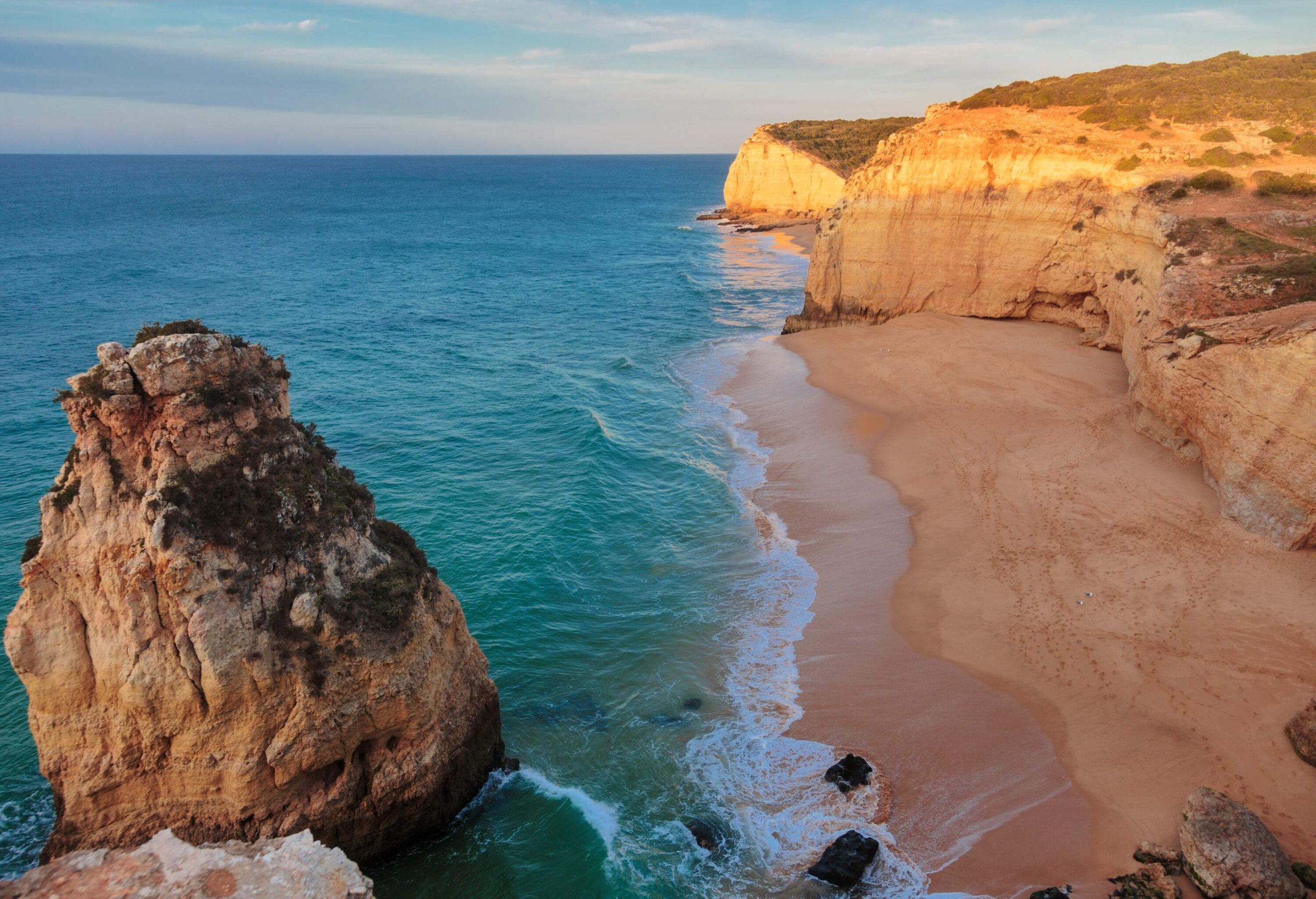 An empty beach with towering cliffs lining its coast.