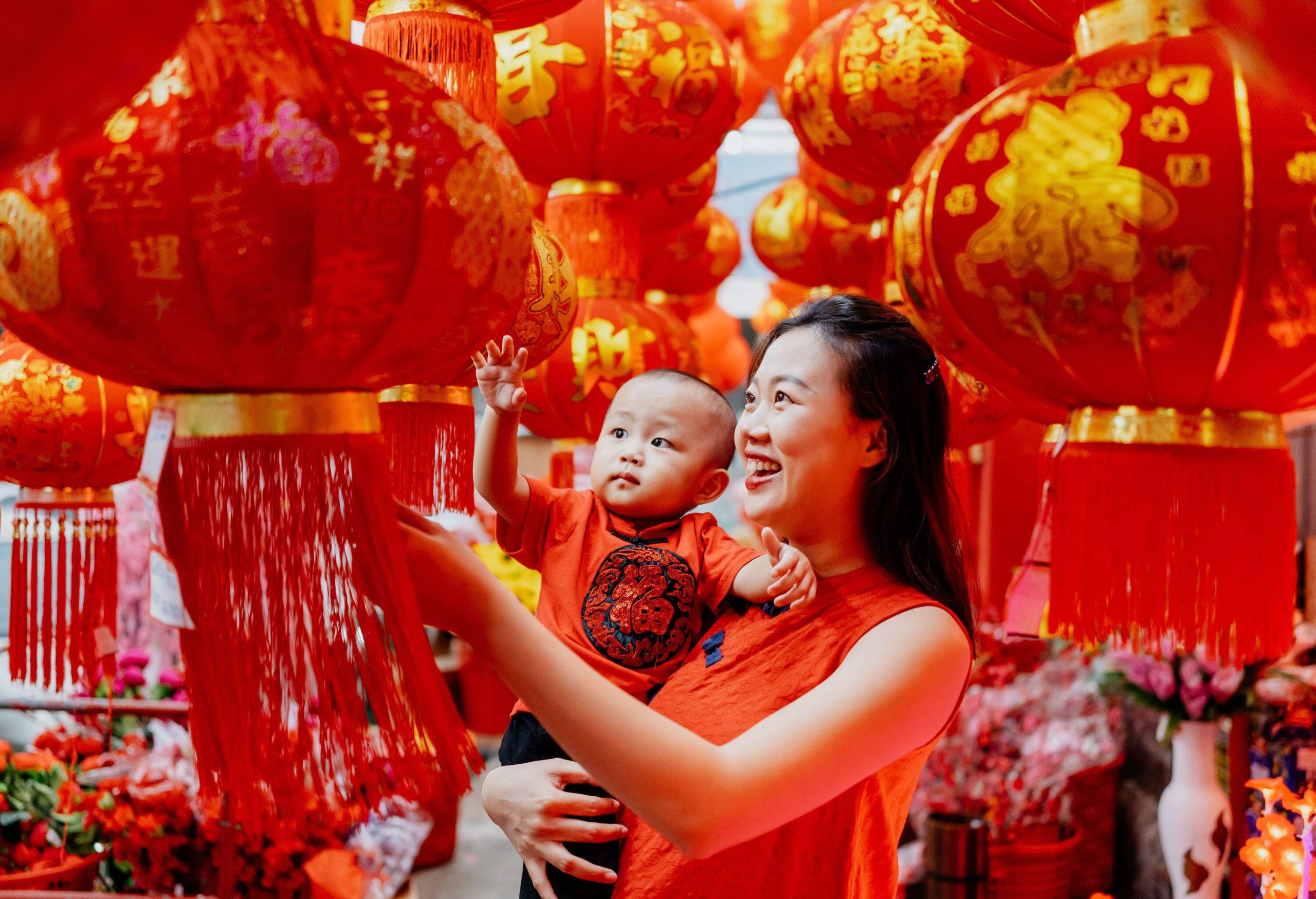 An Asian Chinese mother carrying her baby shopping and looking for red lantern for Chinese new year decoration