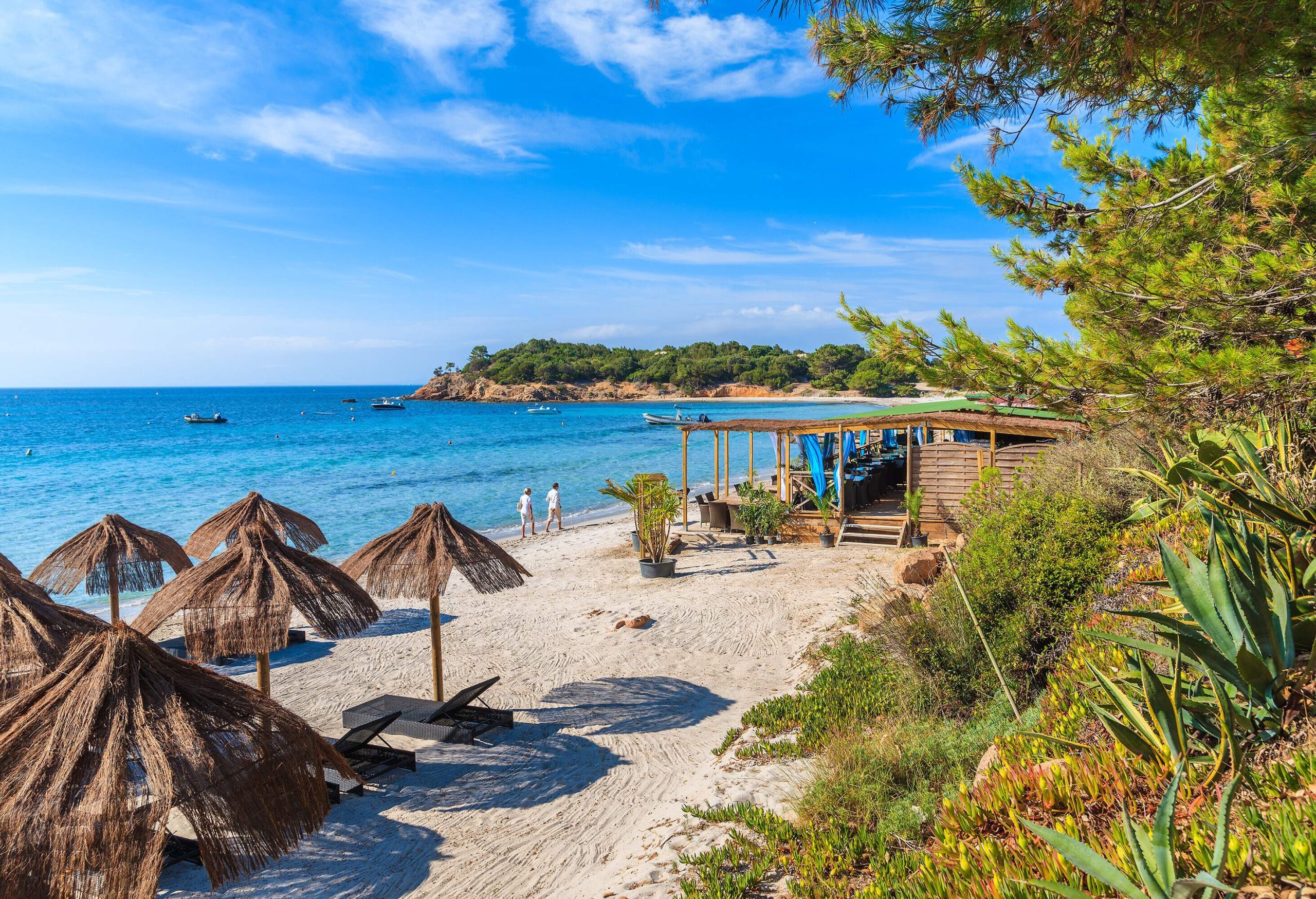 Two people walking by bungalow restaurant on the beach.