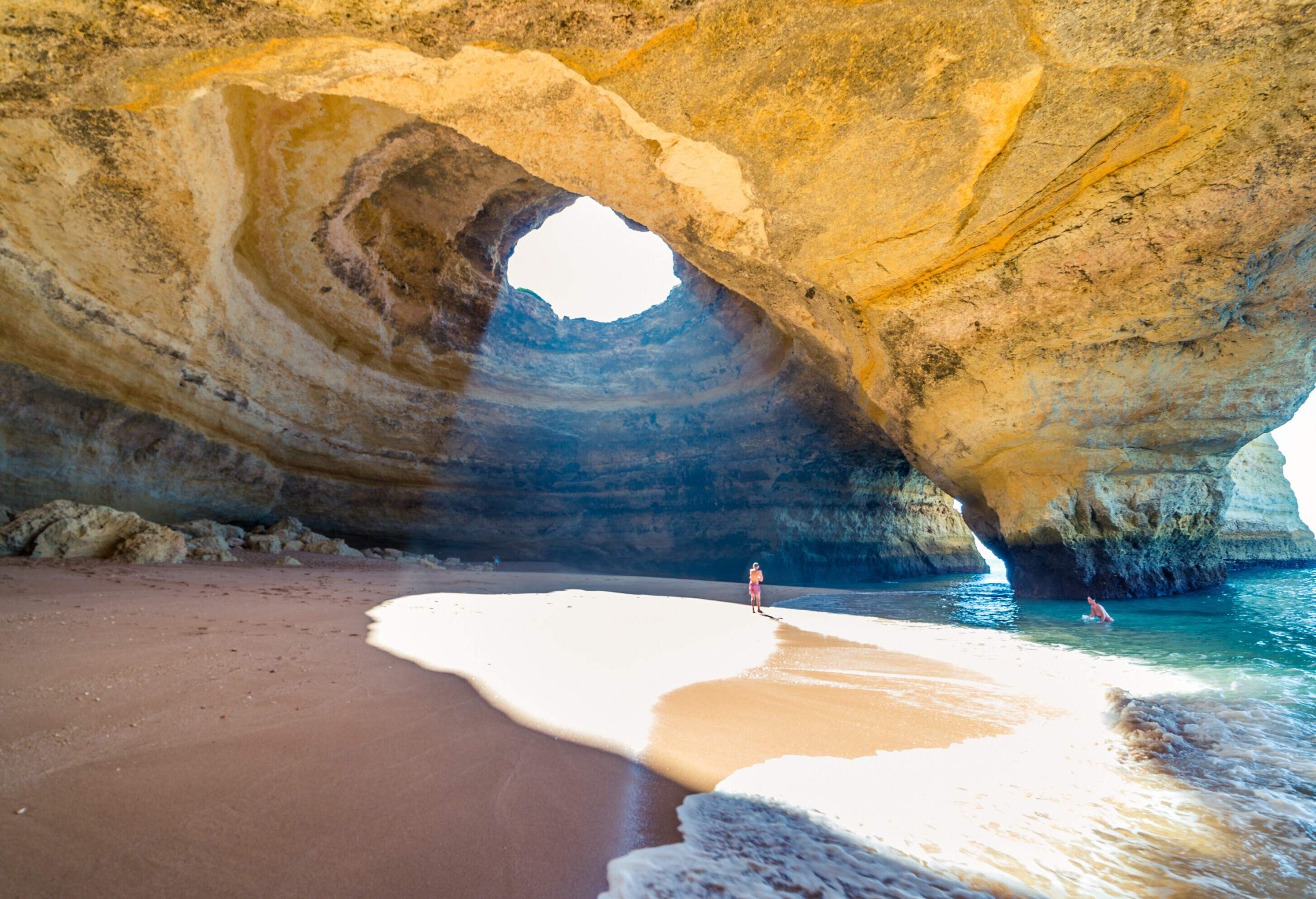People are swimming on the beach below the cave and basking in the sun through the keyhole.