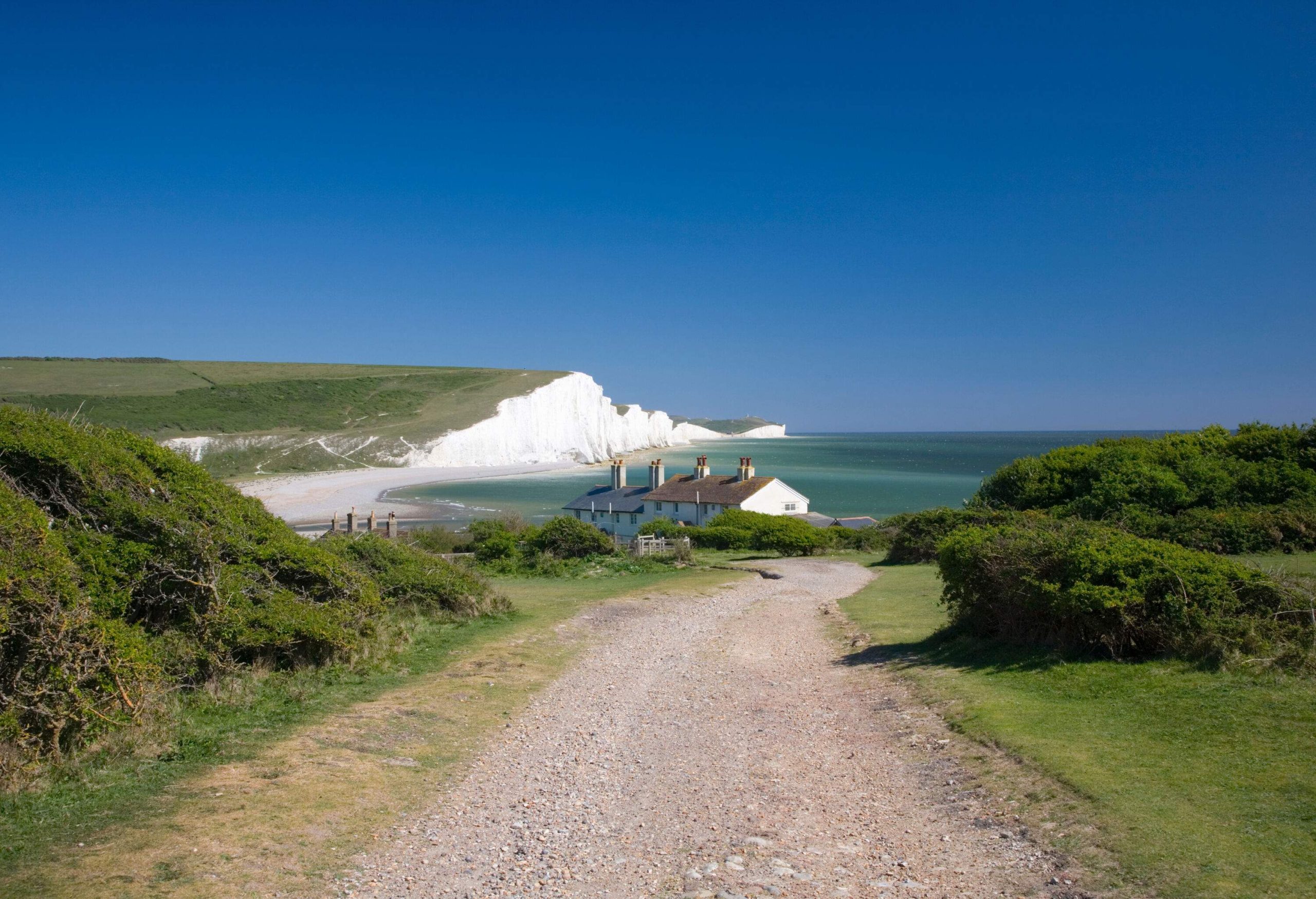 A gravel road down to the beach bordered by chalk sea cliffs.