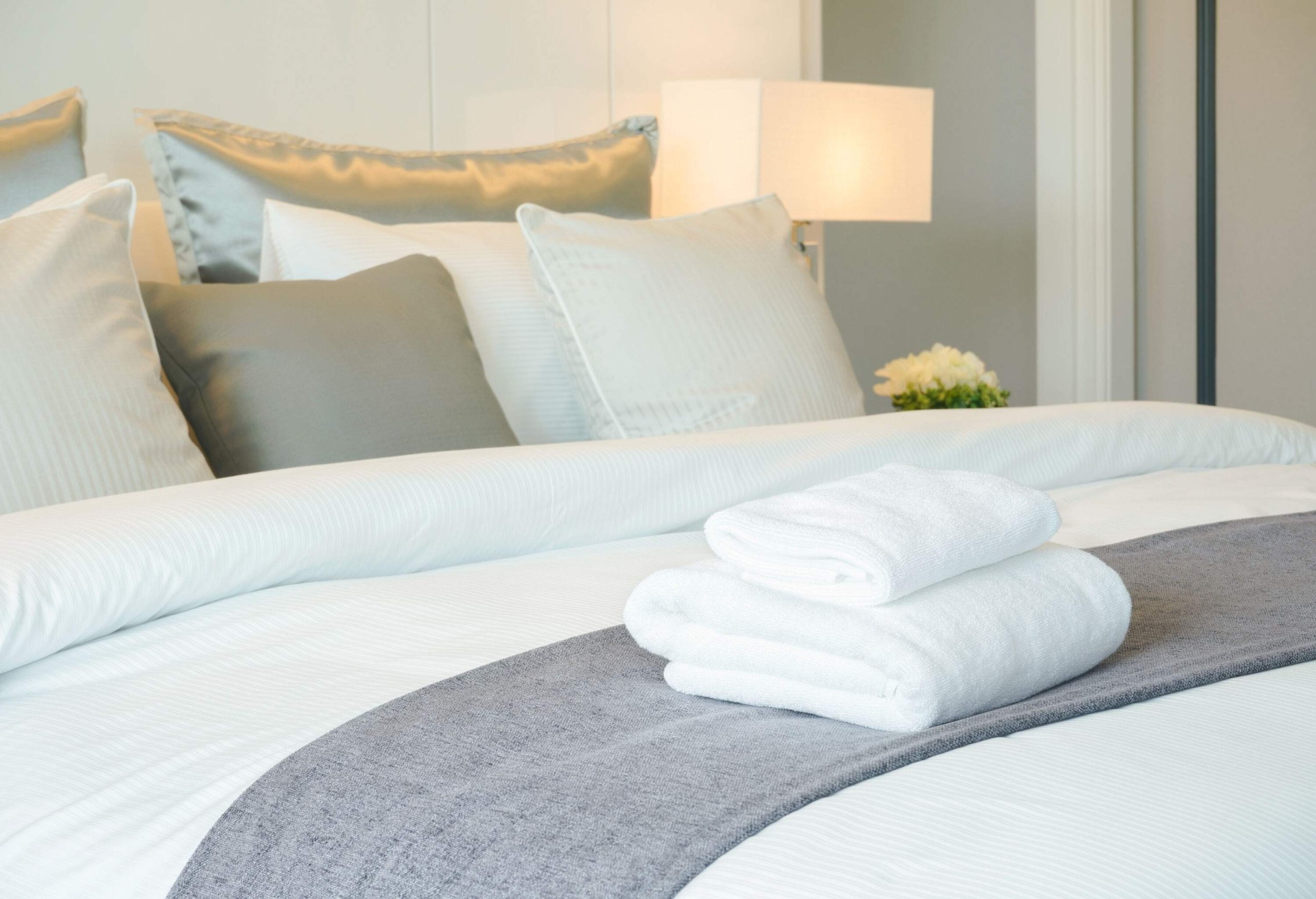A bed with decorative pillows against the headboard and folded white towels over the duvet.