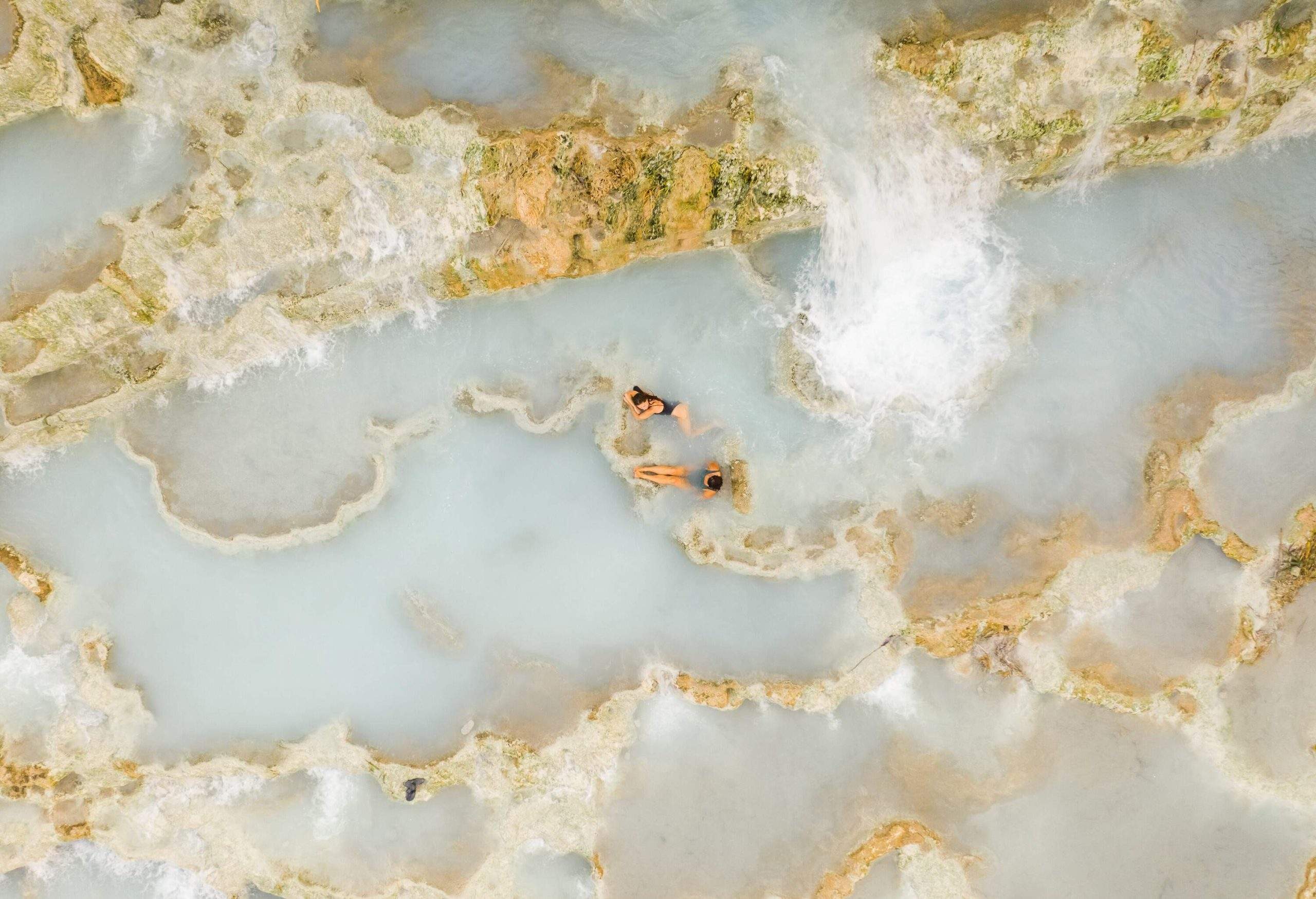 Two women bask in the serene milky waters of Terme di Saturnia, indulging in the luxurious and therapeutic experience of the renowned hot springs.