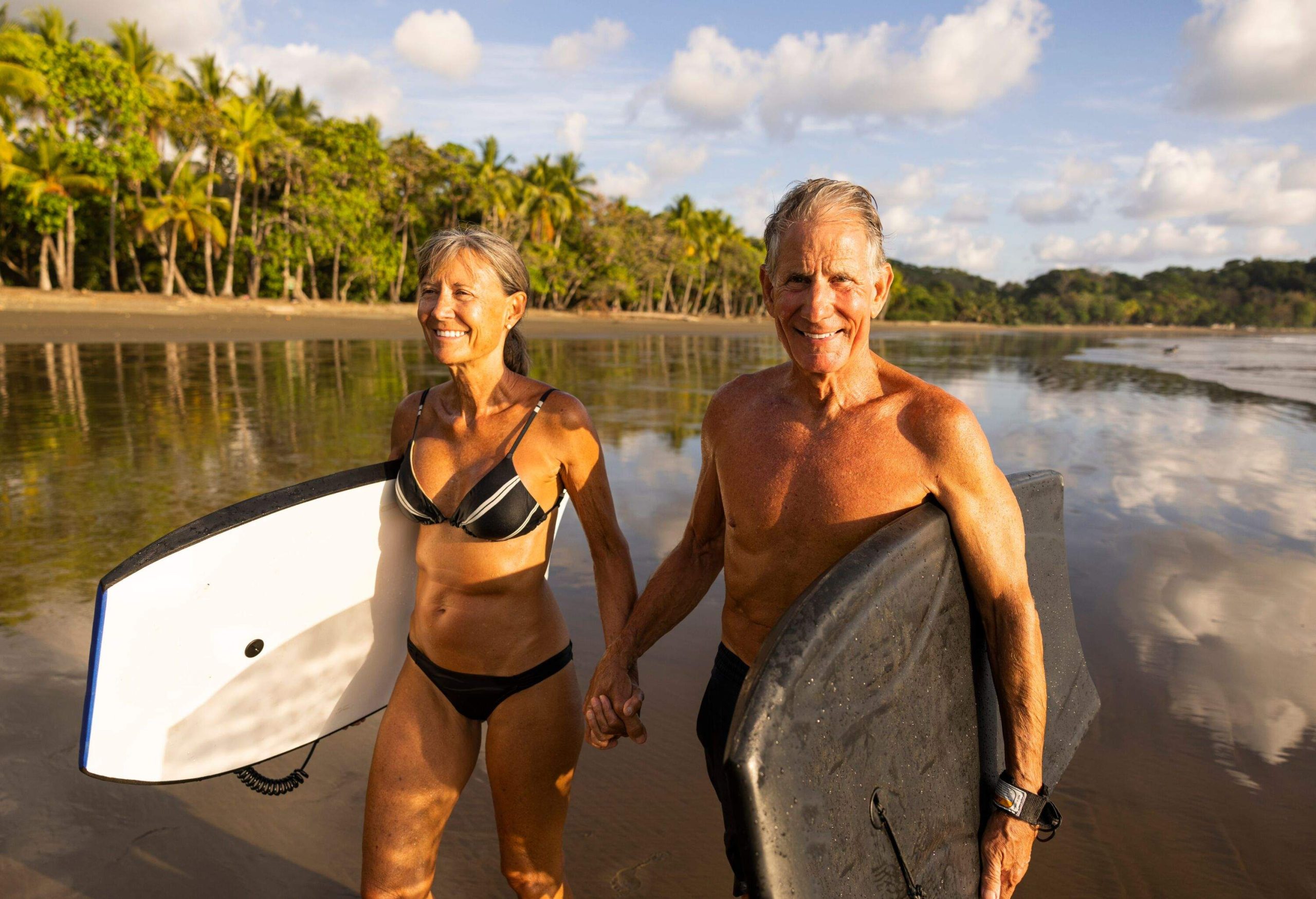 senior couple holding hands and stand up paddles on a tropical beach