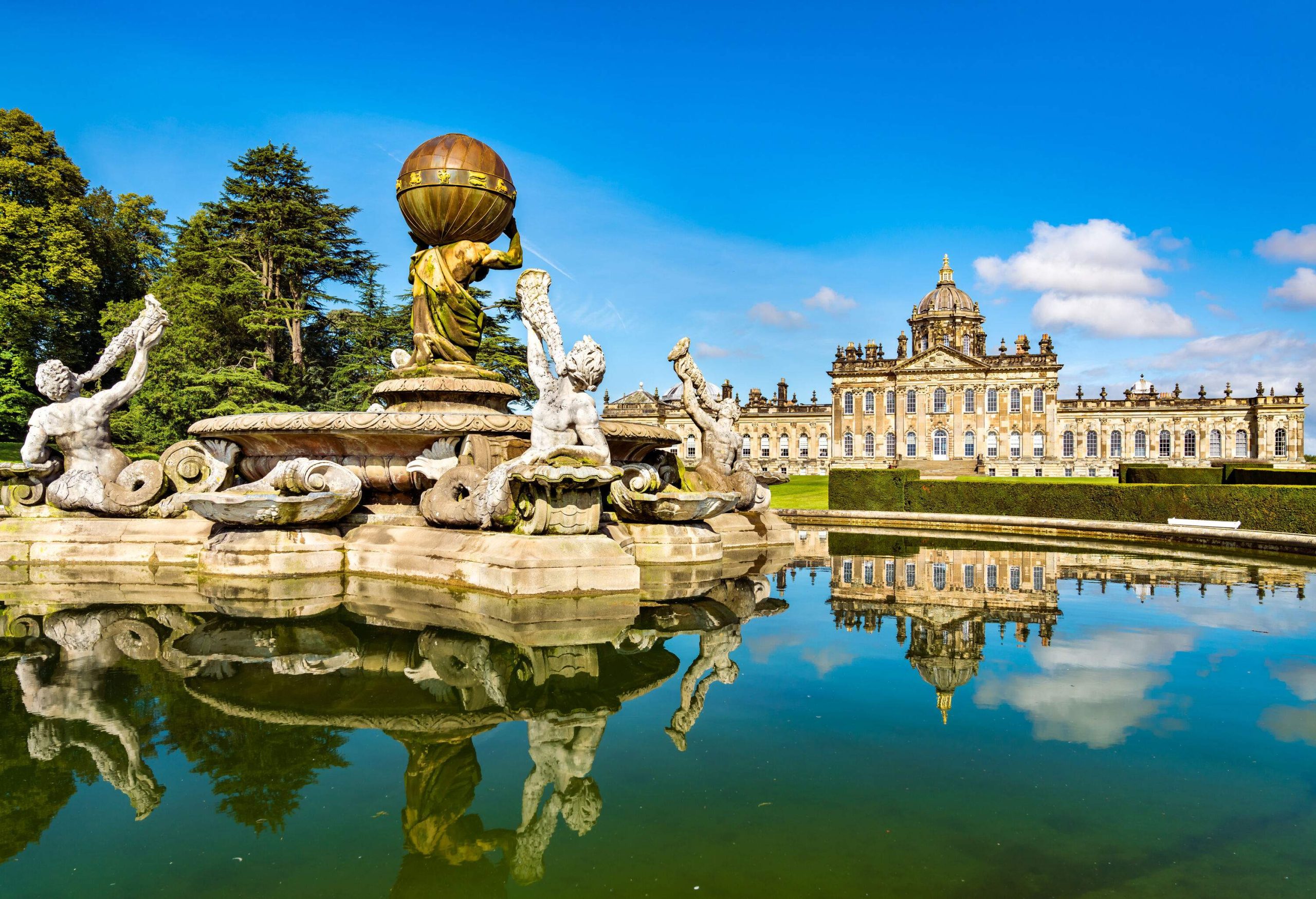 A large bronze globe dominates a fountain in the middle of a circular pond on a grassy lawn with a castle in the background.