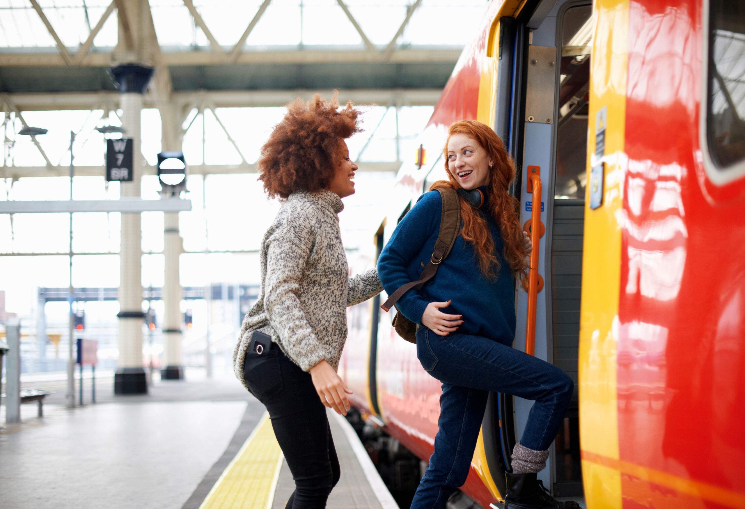 Two women passengers talking while boarding a colourful train in the station.