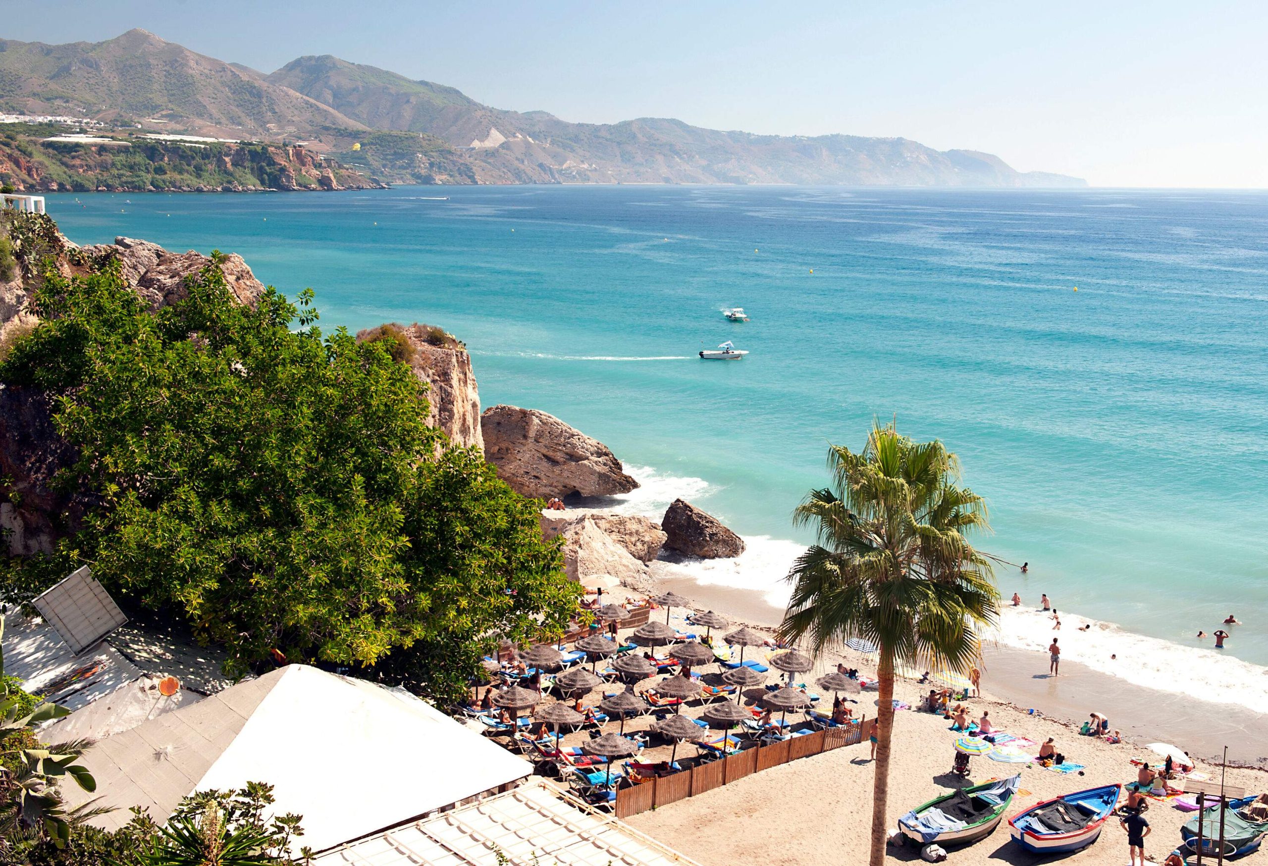 A stunning beach with umbrellas and boats on the sand, as well as people swimming in the clear blue water.