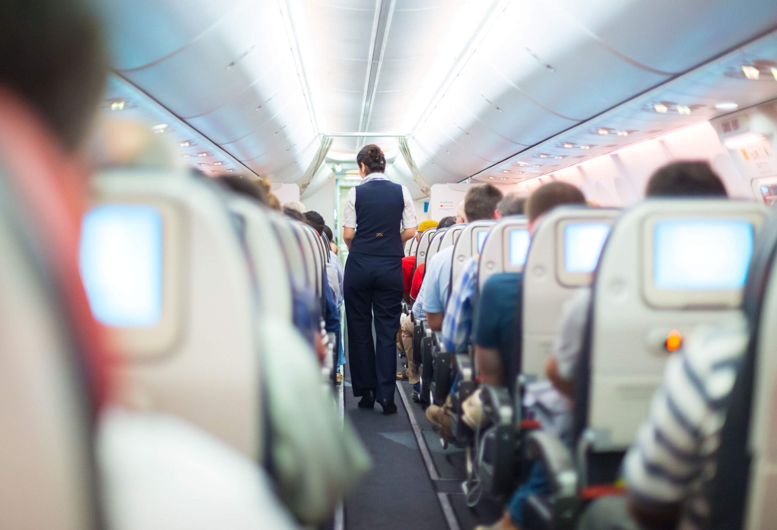A flight attendant walking through the aisle of an airplane between passengers.