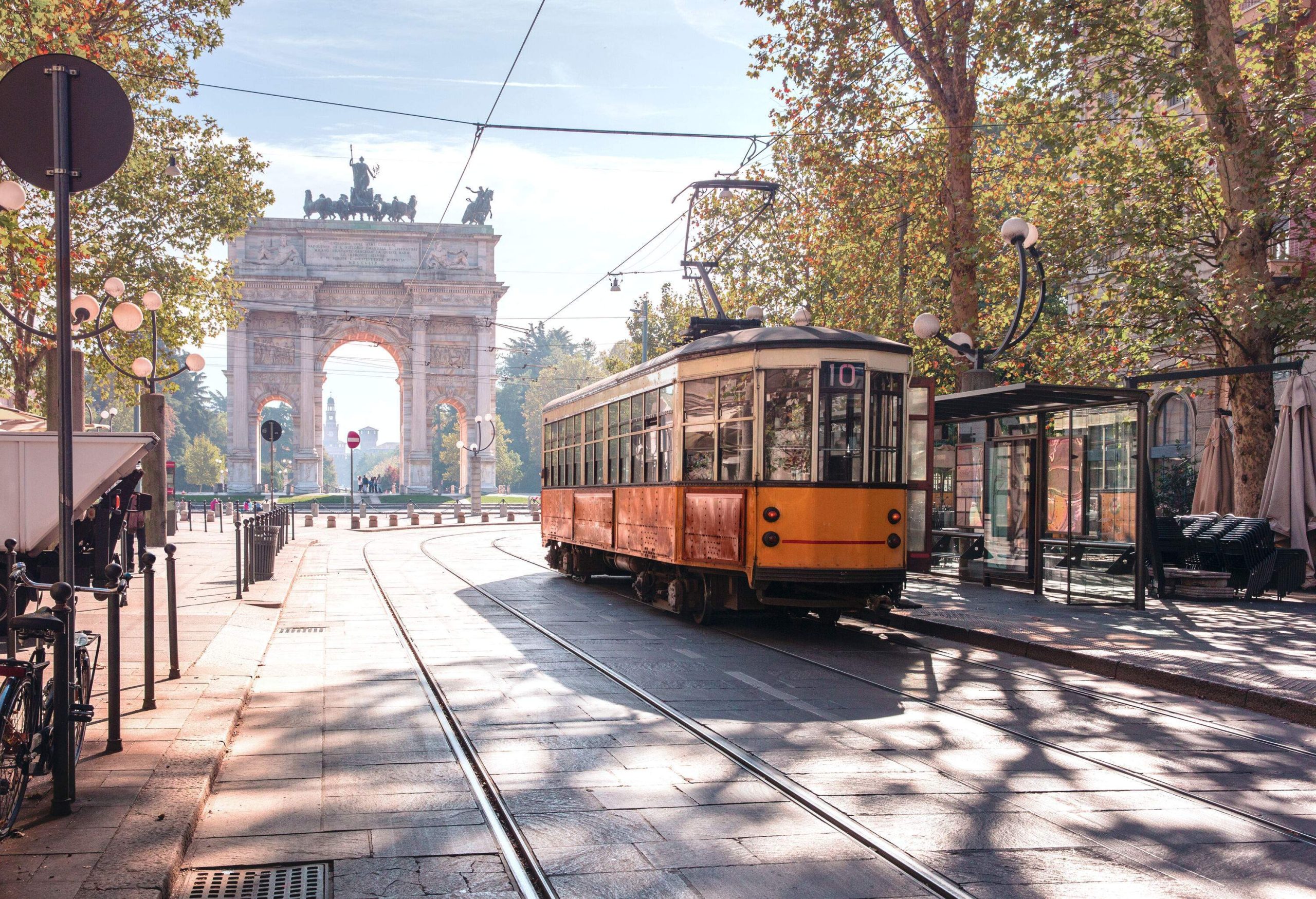 A vintage tram in the centre of an old town against a triumphal arch with bas-reliefs and statues on top.