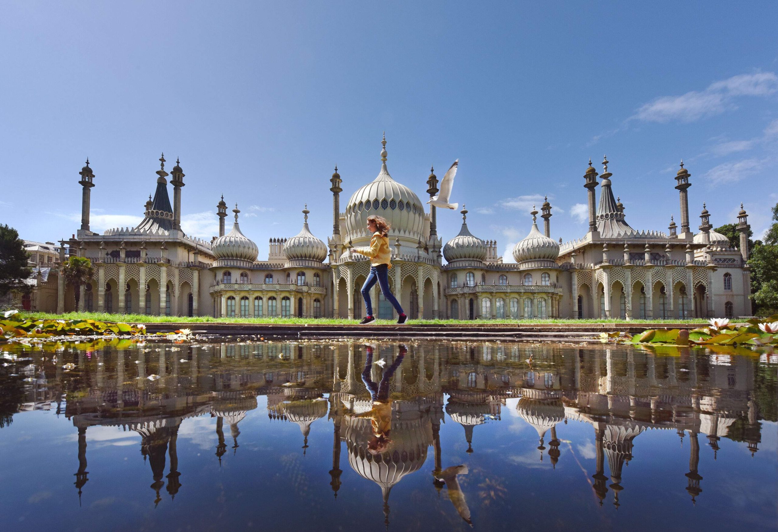 A girl runs alongside a pond with the Brighton Pavilion mirrored on its surface.