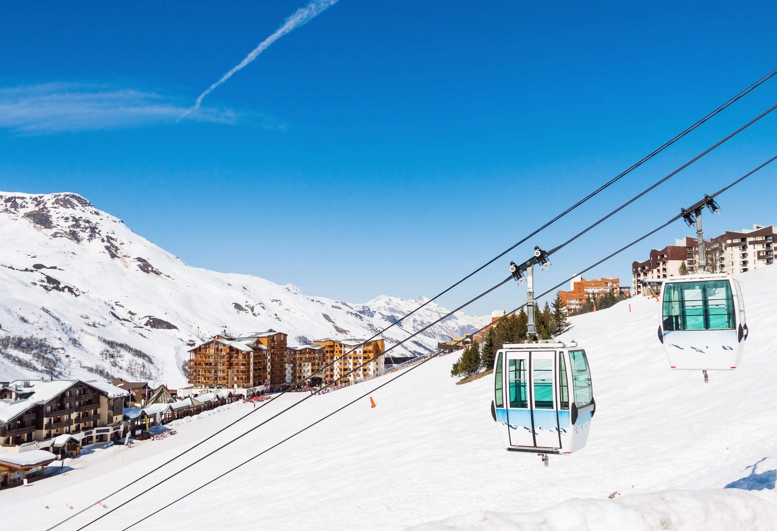 Two cable cars suspended above a snow hill with views of a ski village at the base of a mountain.