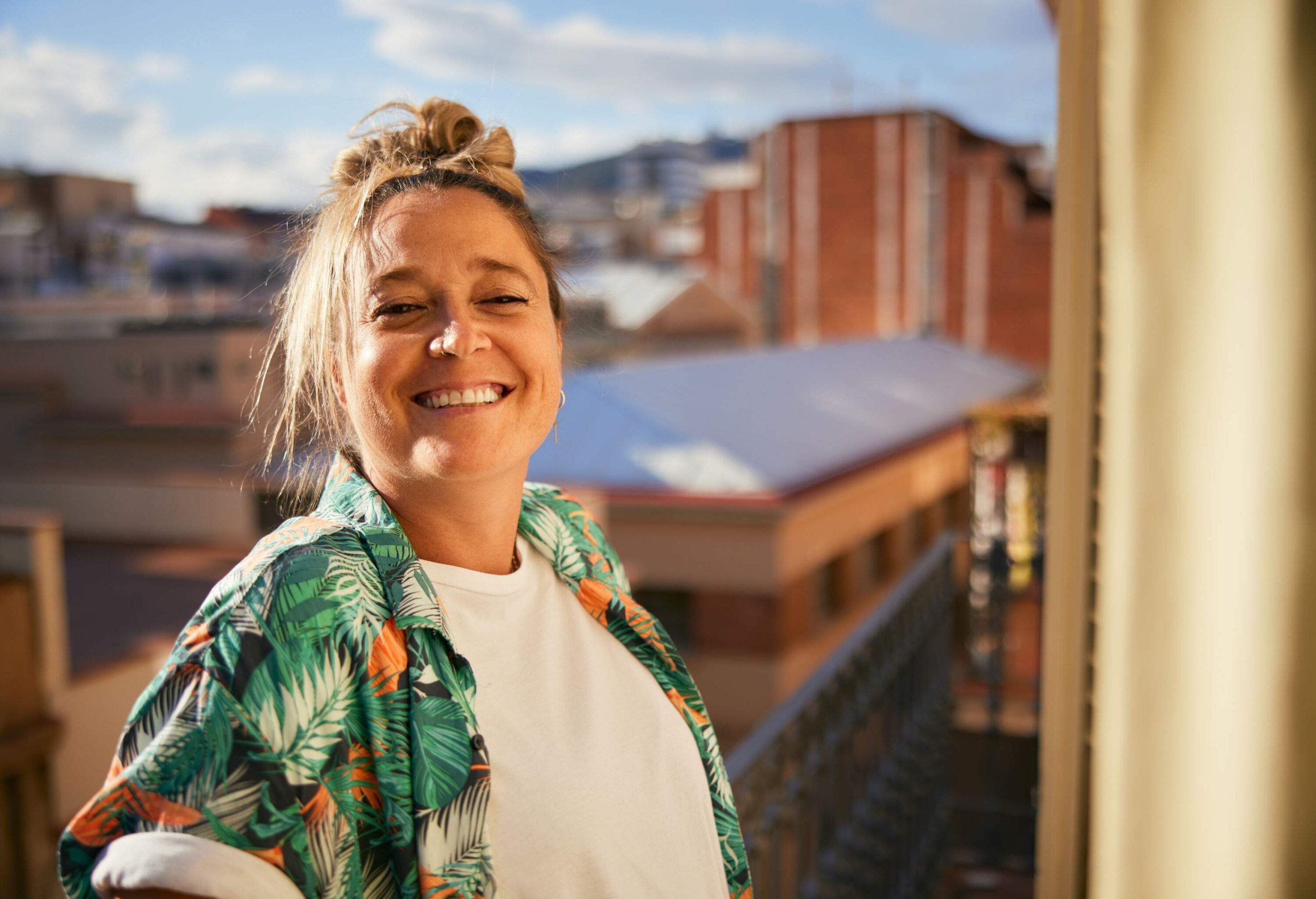 On the balcony, a woman smiles at the camera with a happy expression.