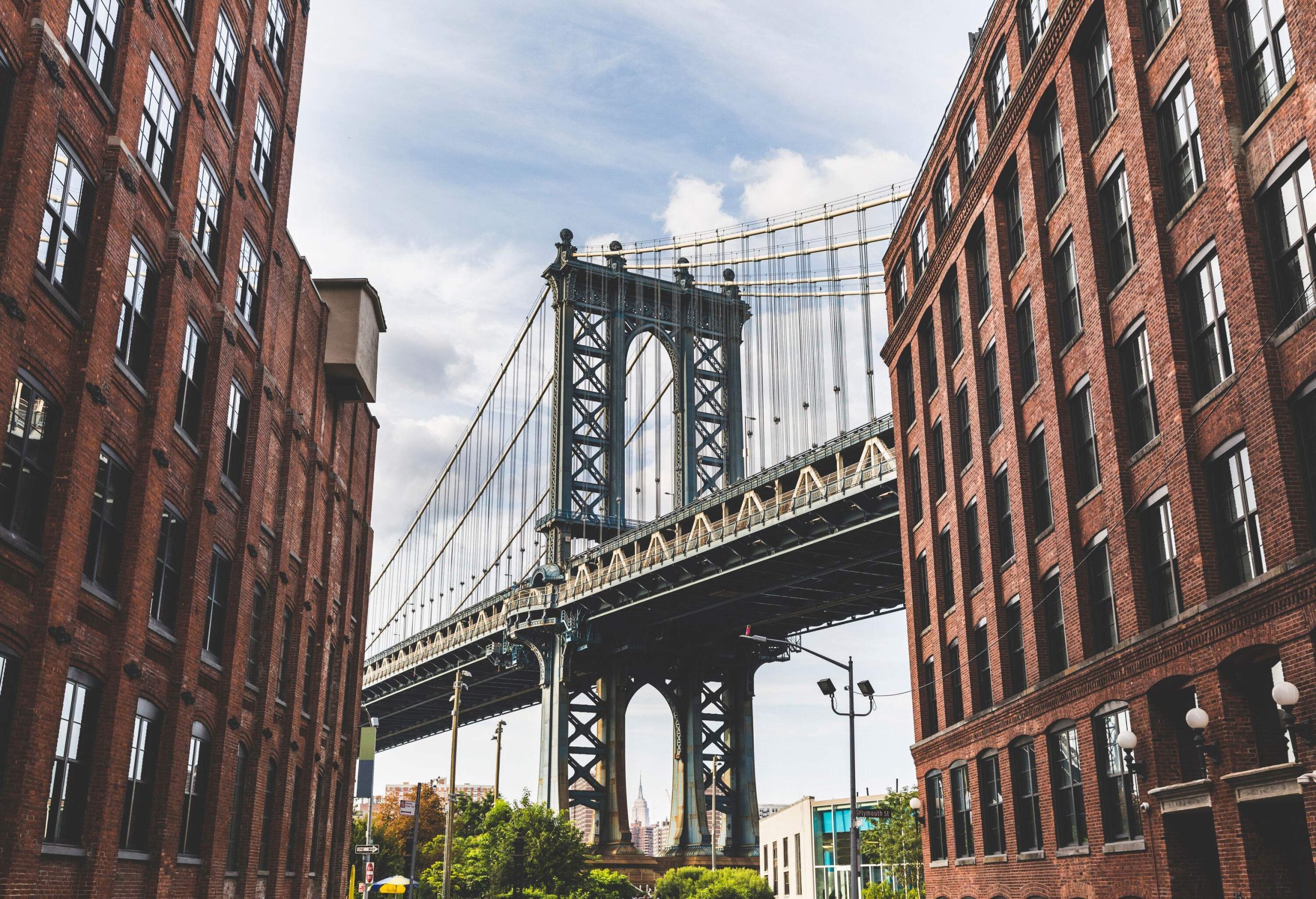 The Manhattan Bridge framed by brownstone warehouse buildings on the side of the street.