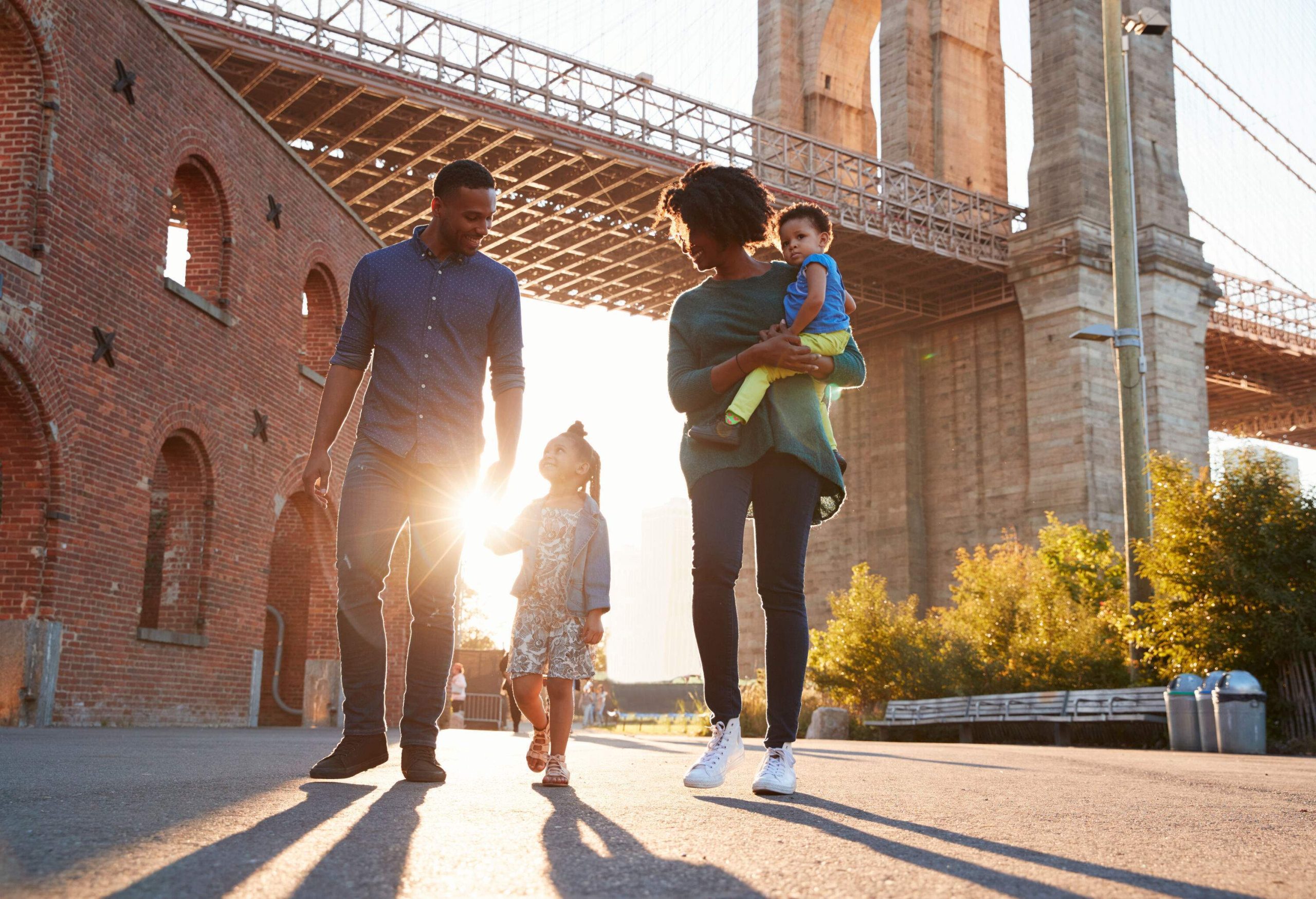 A family of four strolling down the street with a huge bridge behind them.