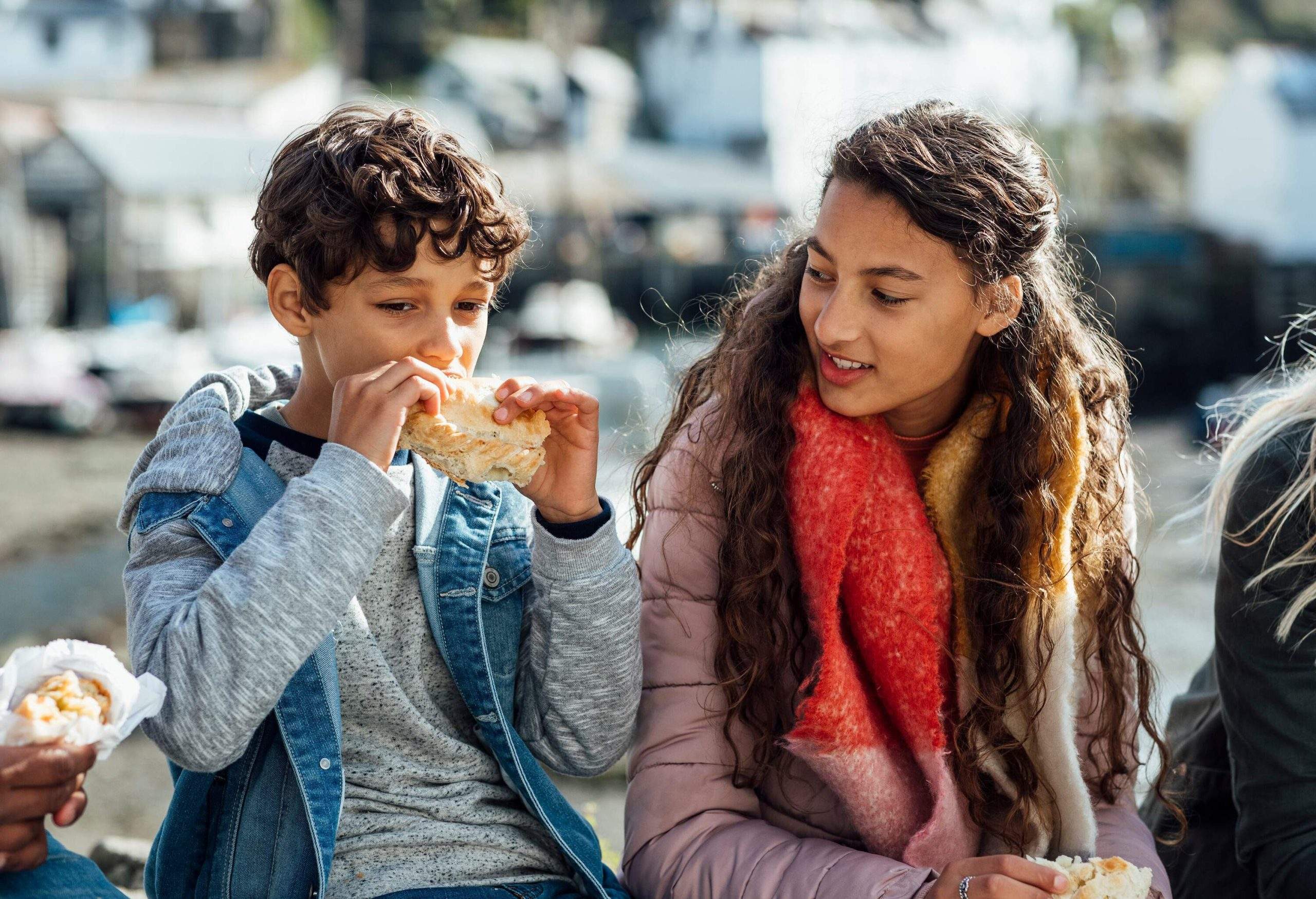 A boy and a girl sit next to each other, the boy eating a snack while the girl watches.