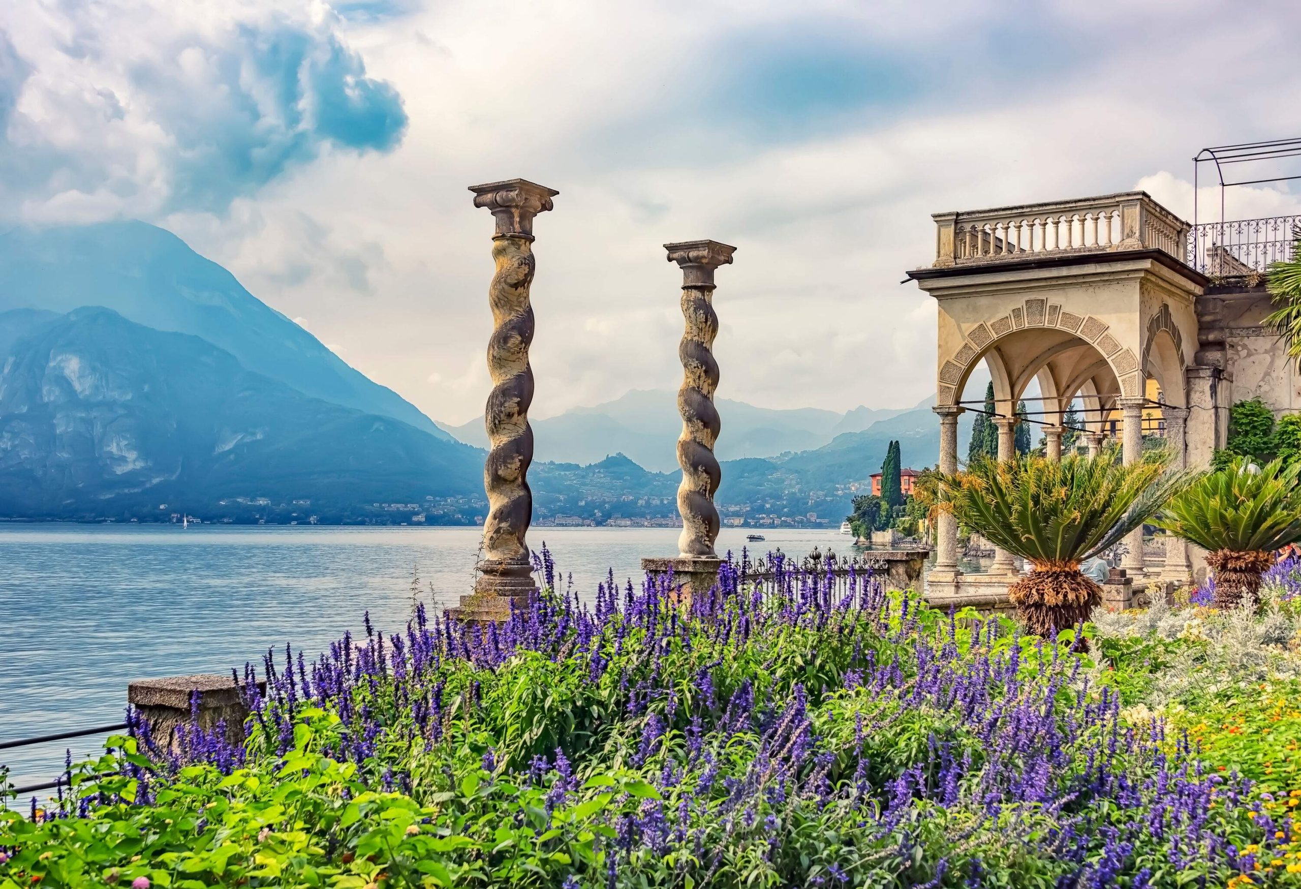 A balcony overlooks a colourful garden with two twisted columns beside a big lake.