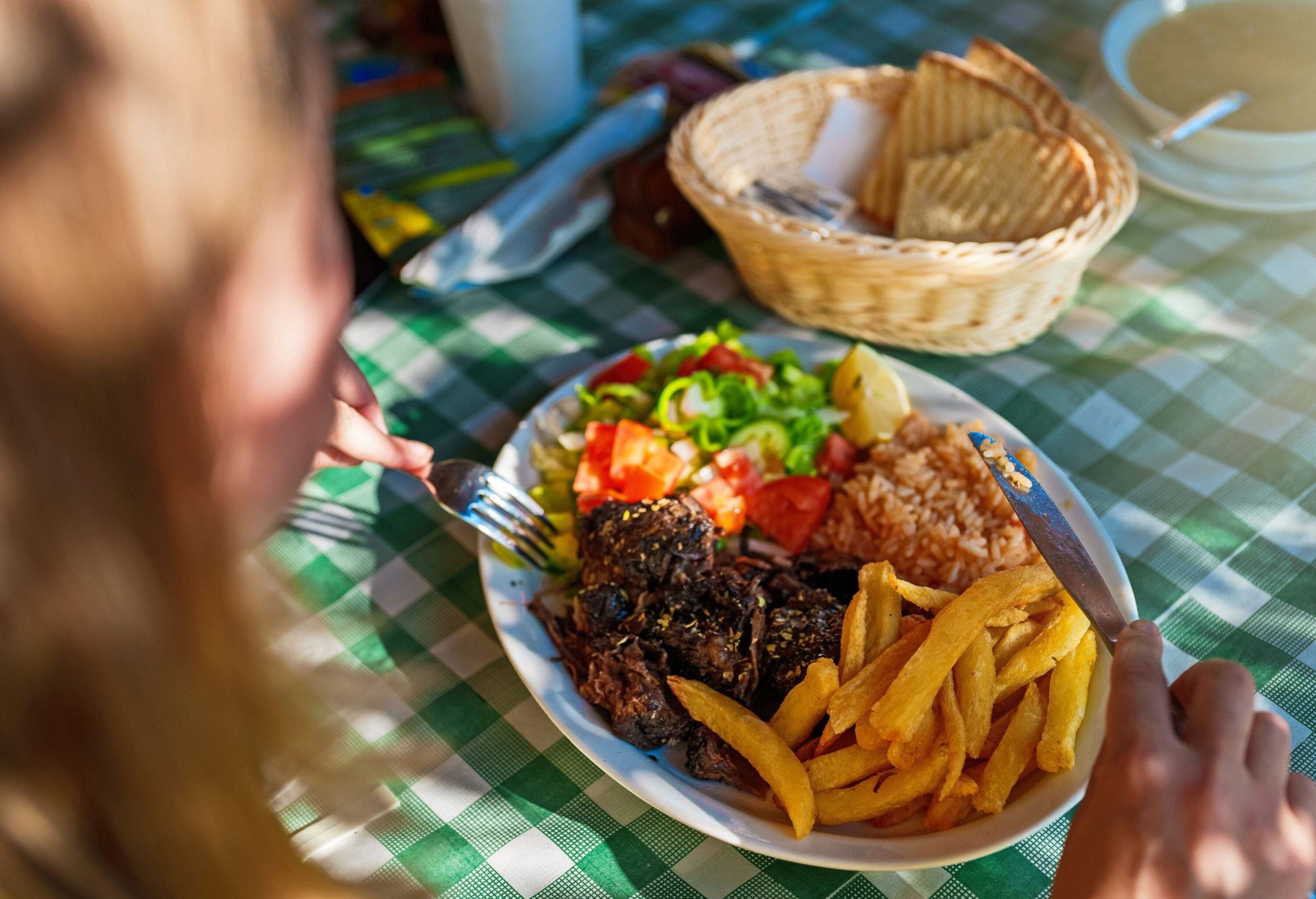 An individual eating a traditional Greek beef stifado with rice, french fries and vegetable salad on the side.