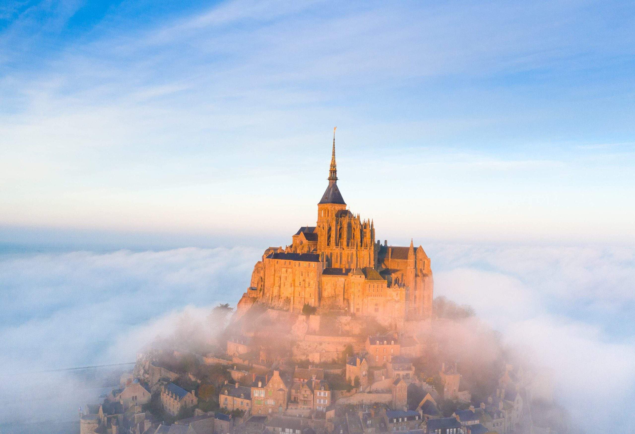 The island of Mont Saint-Michel is blanketed in mist except for the prominent abbey perched on its summit.