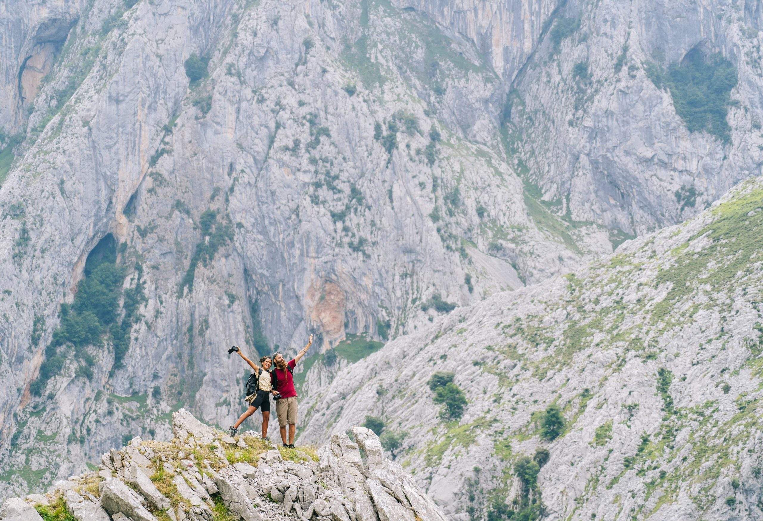 A couple standing on a mountain's crest with their hands raised.