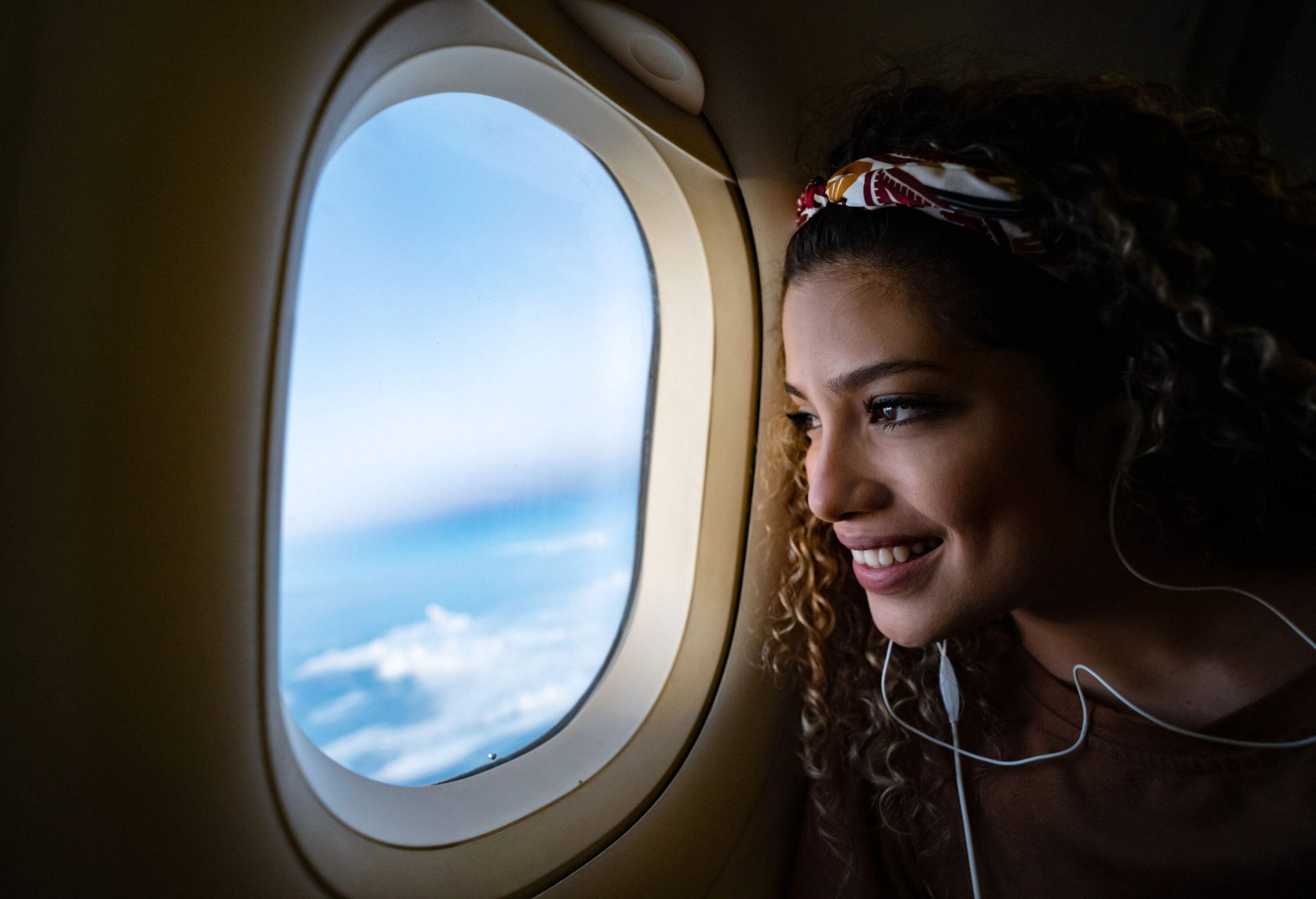 A curly-haired woman smiles as she looks out the airplane window.