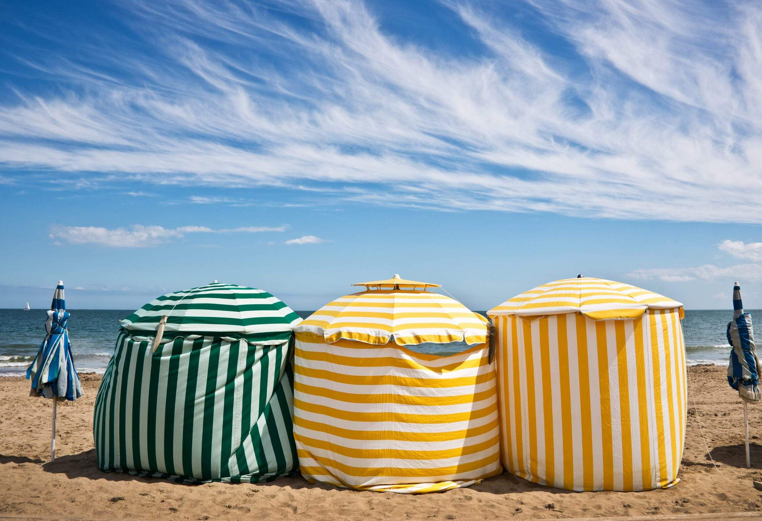 Colourful striped tents standing on golden sand along the shore.