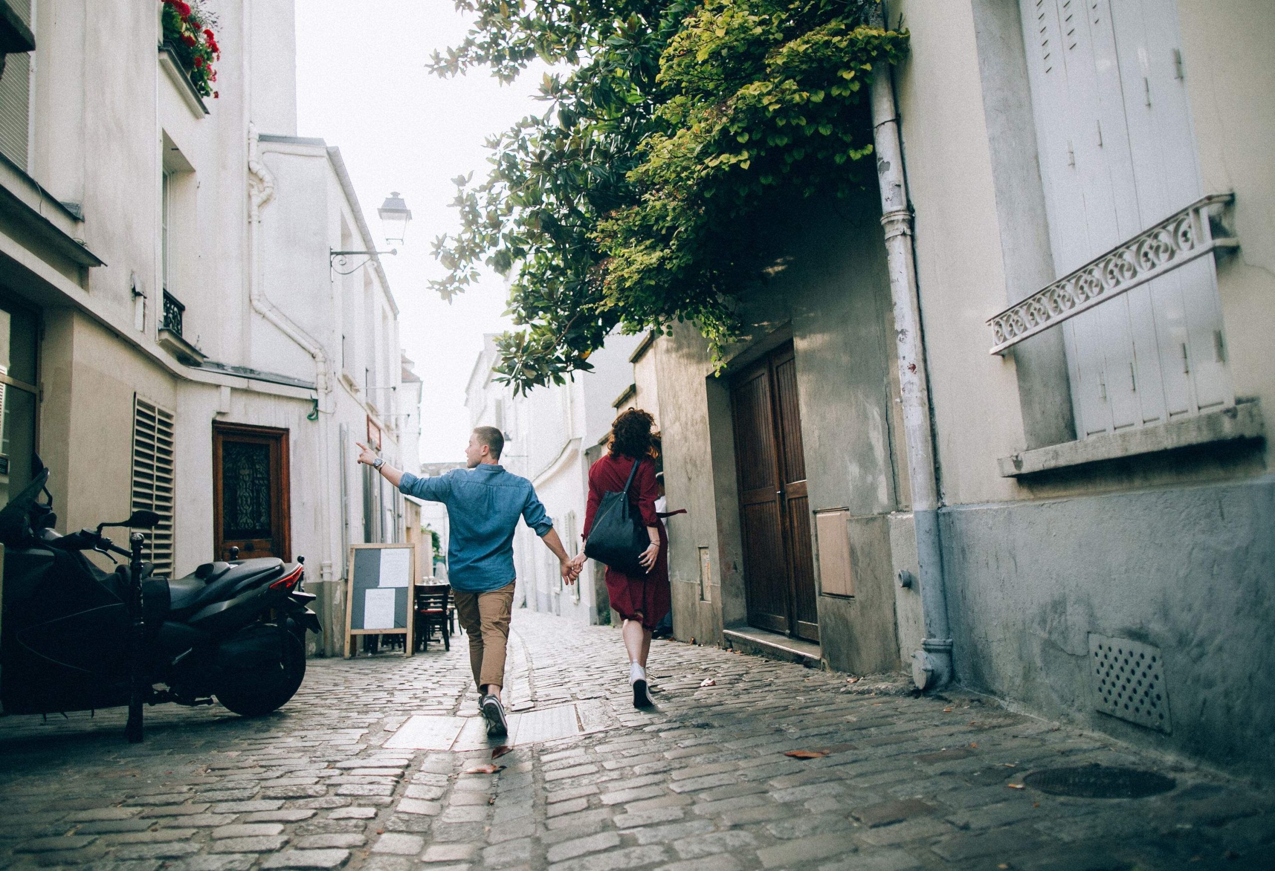 A couple walking hand in hand in a narrow cobbled street lined with old buildings.