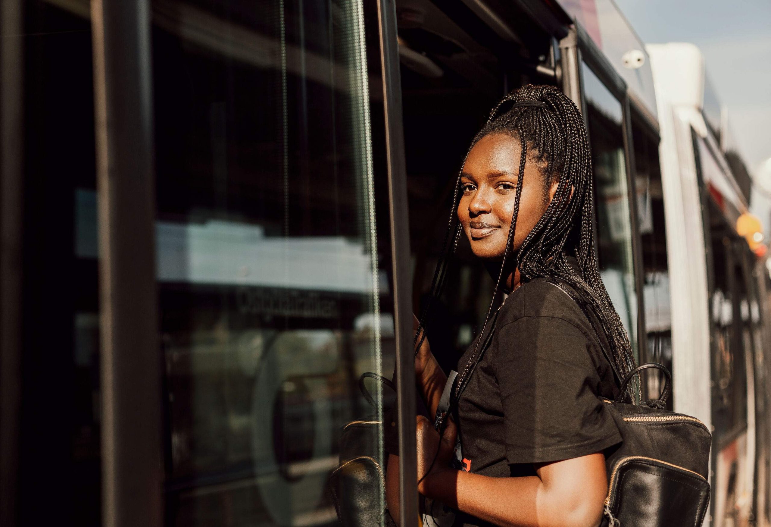 A young girl with braided hair and a black backpack getting on a train.