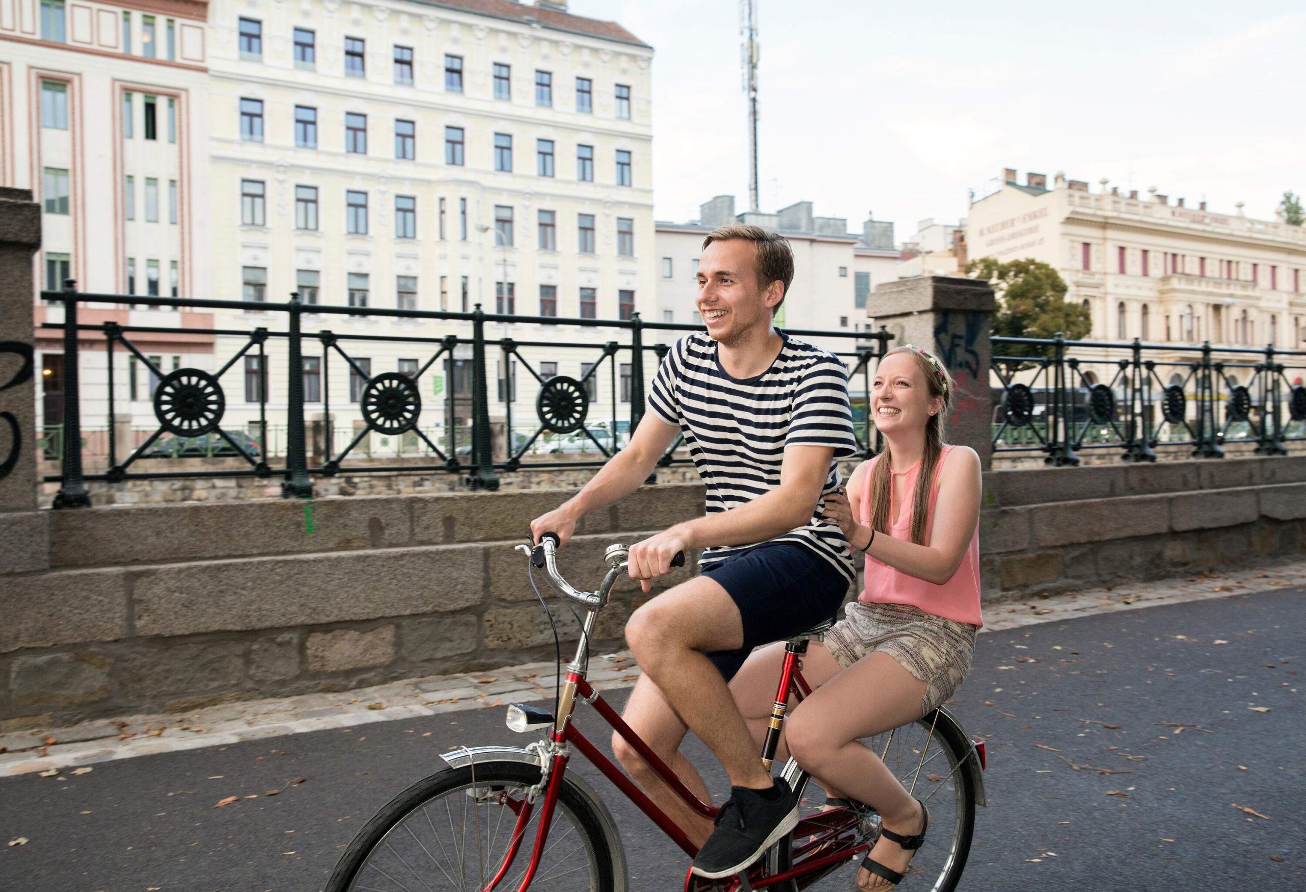 A delightful couple pedals together on a bicycle, enjoying a shared adventure and the beauty of their surroundings.