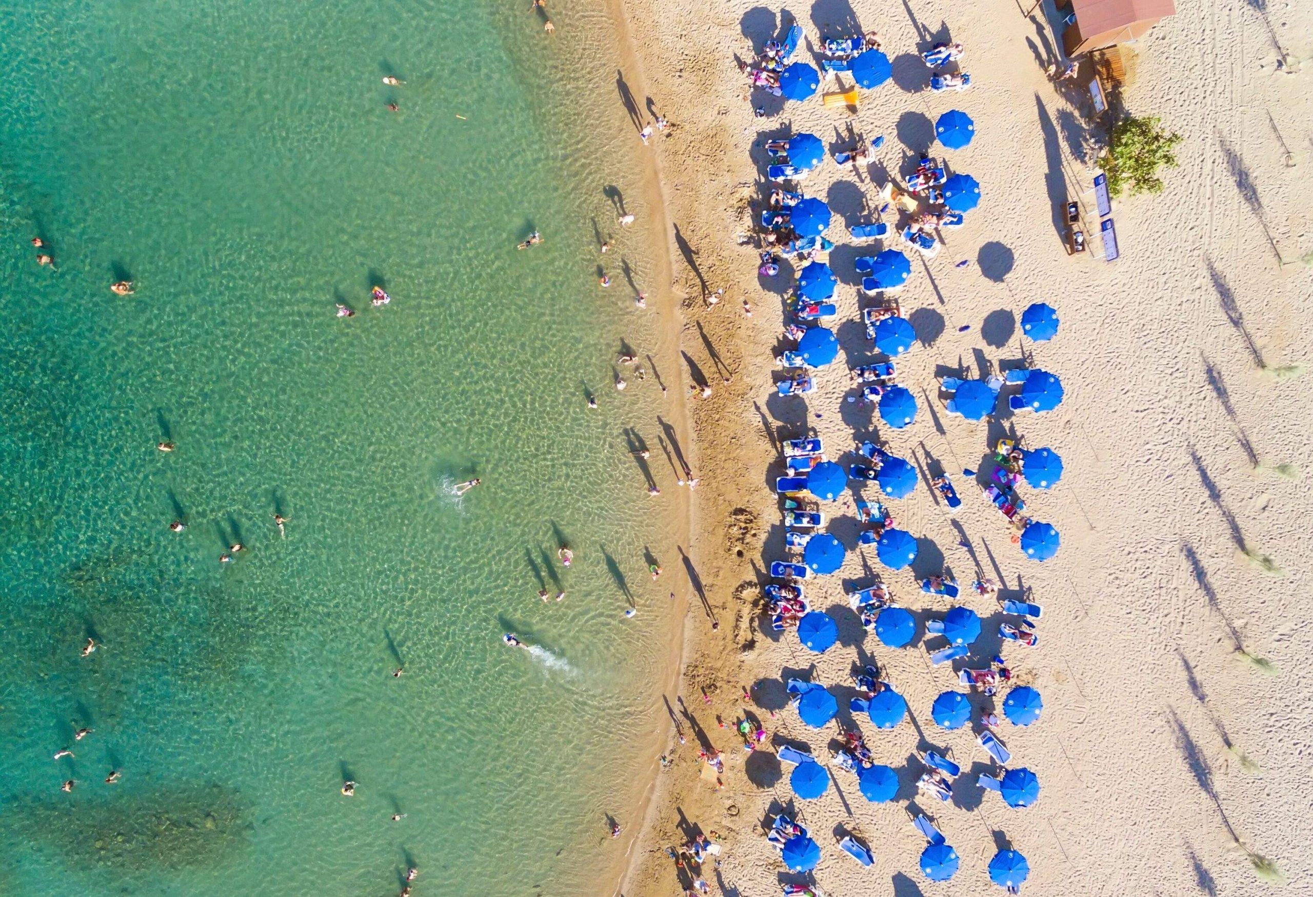 People swimming in an emerald sea with blue umbrellas set on the beach.