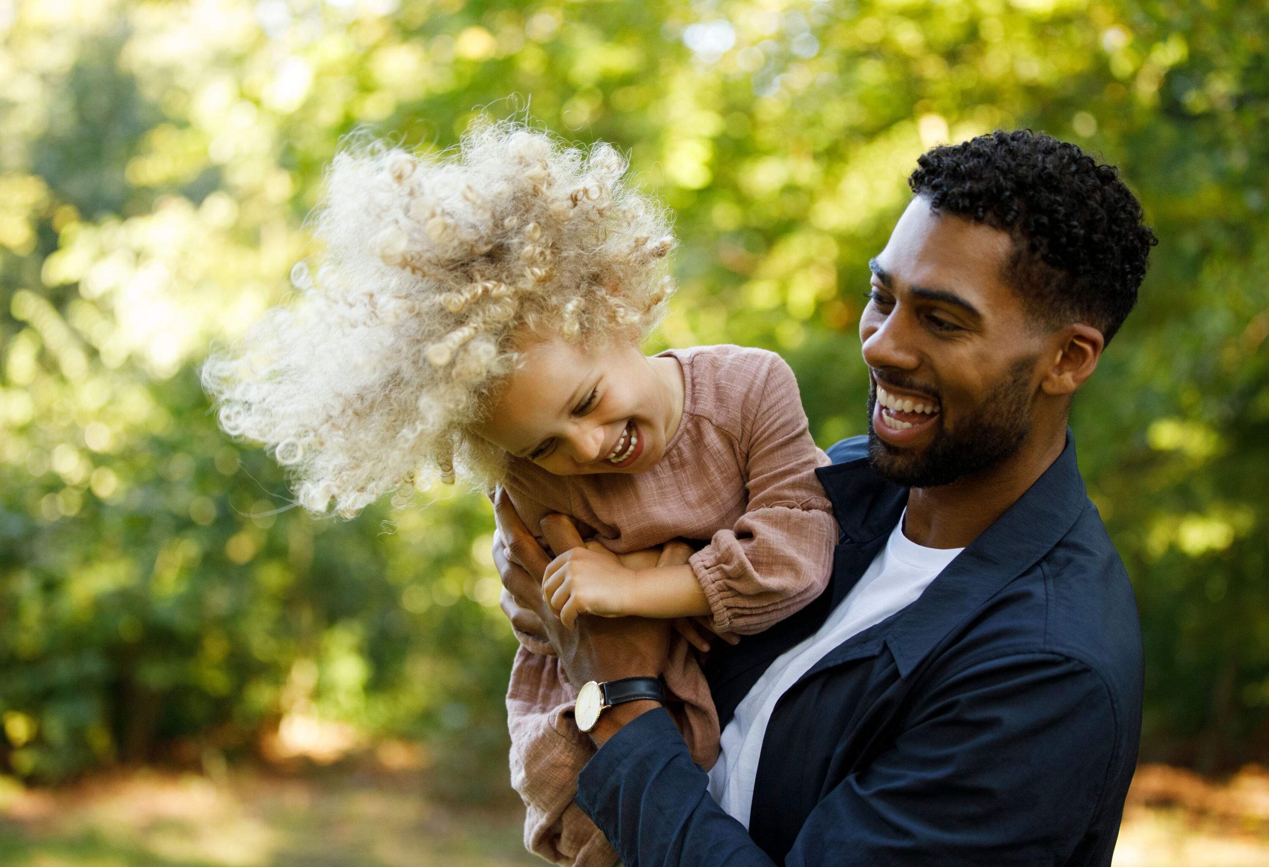 A father carrying his beautiful blonde afro daughter in the park.