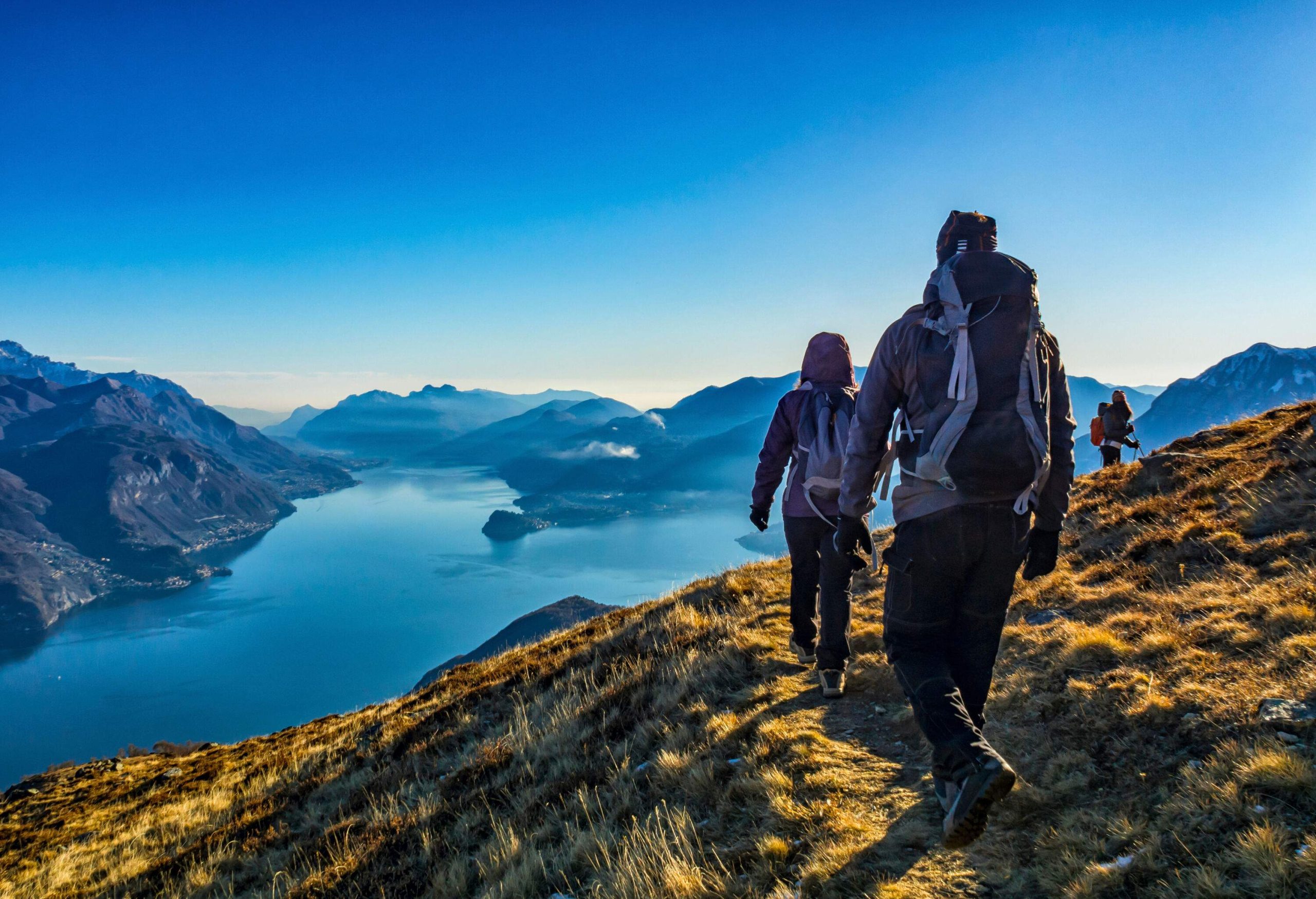 A group of people hiking up a mountain cliff overlooking a lake surrounded by mountains.