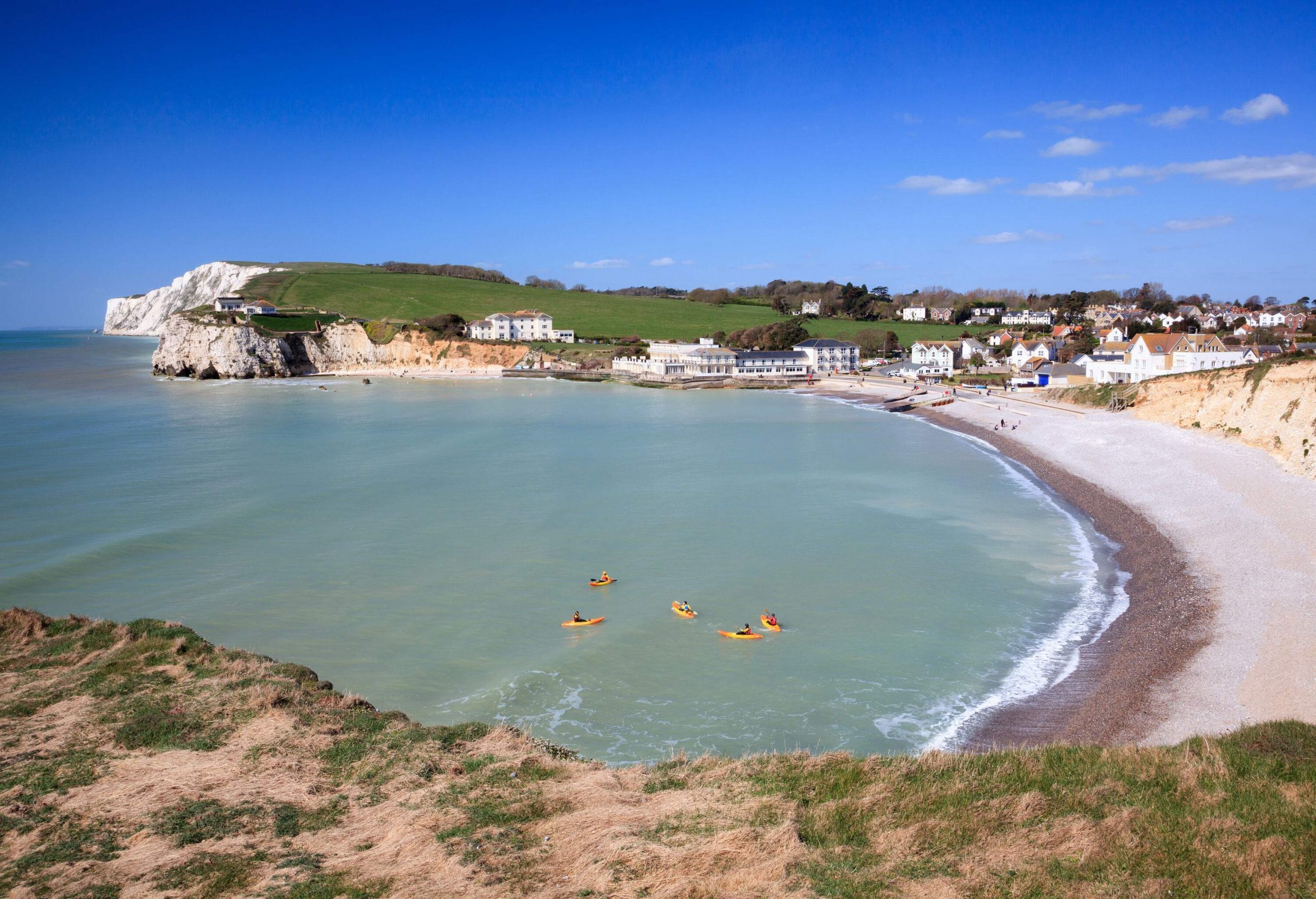 People kayaking in a bay with a curving shoreline and steep cliffs.