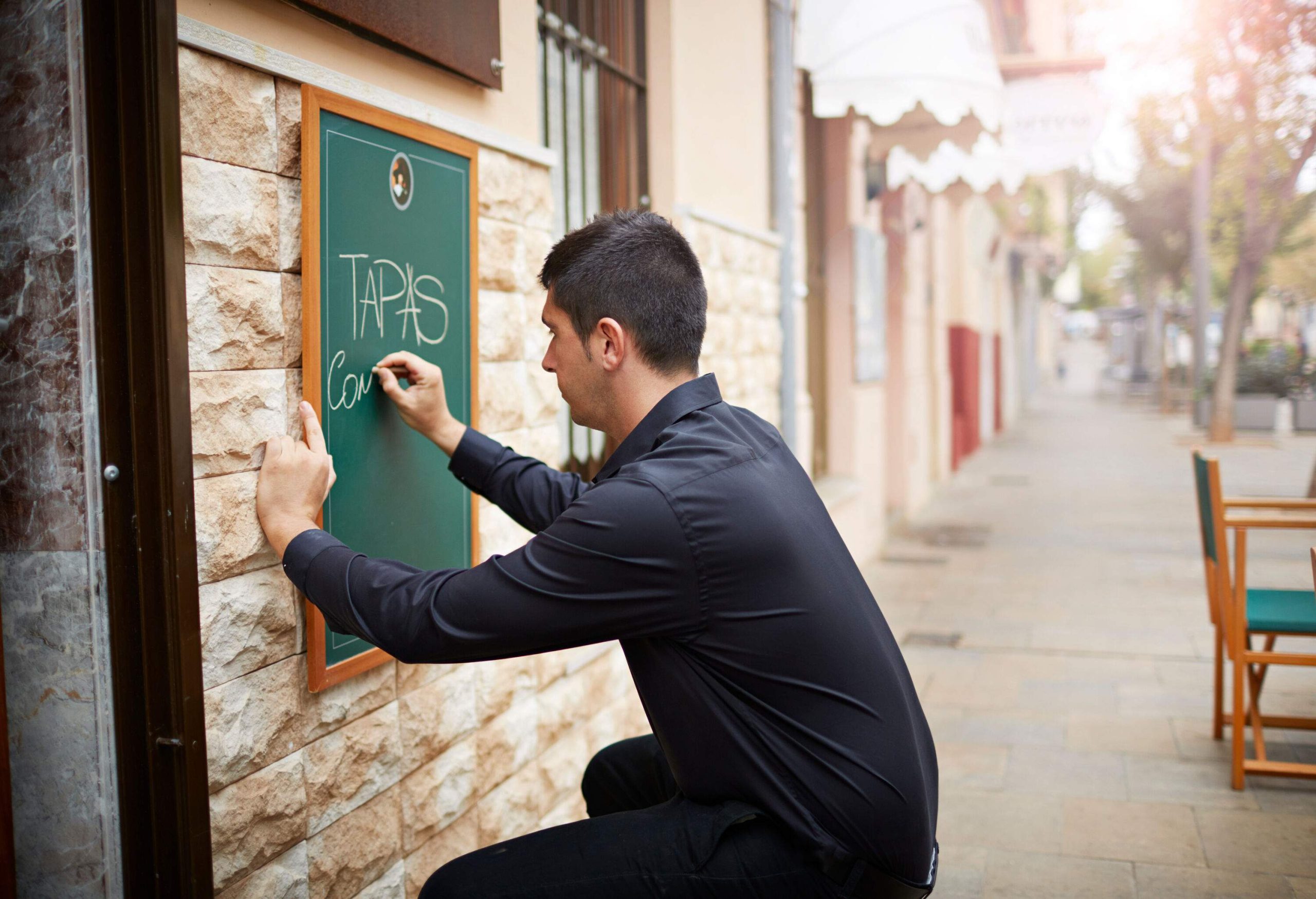 A man in a black long-sleeve writes a menu on a chalkboard.