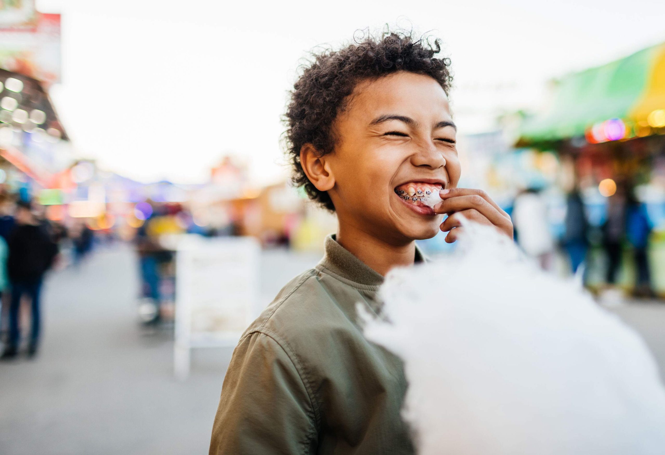 A curly-haired kid with braces eats a piece of cotton candy.