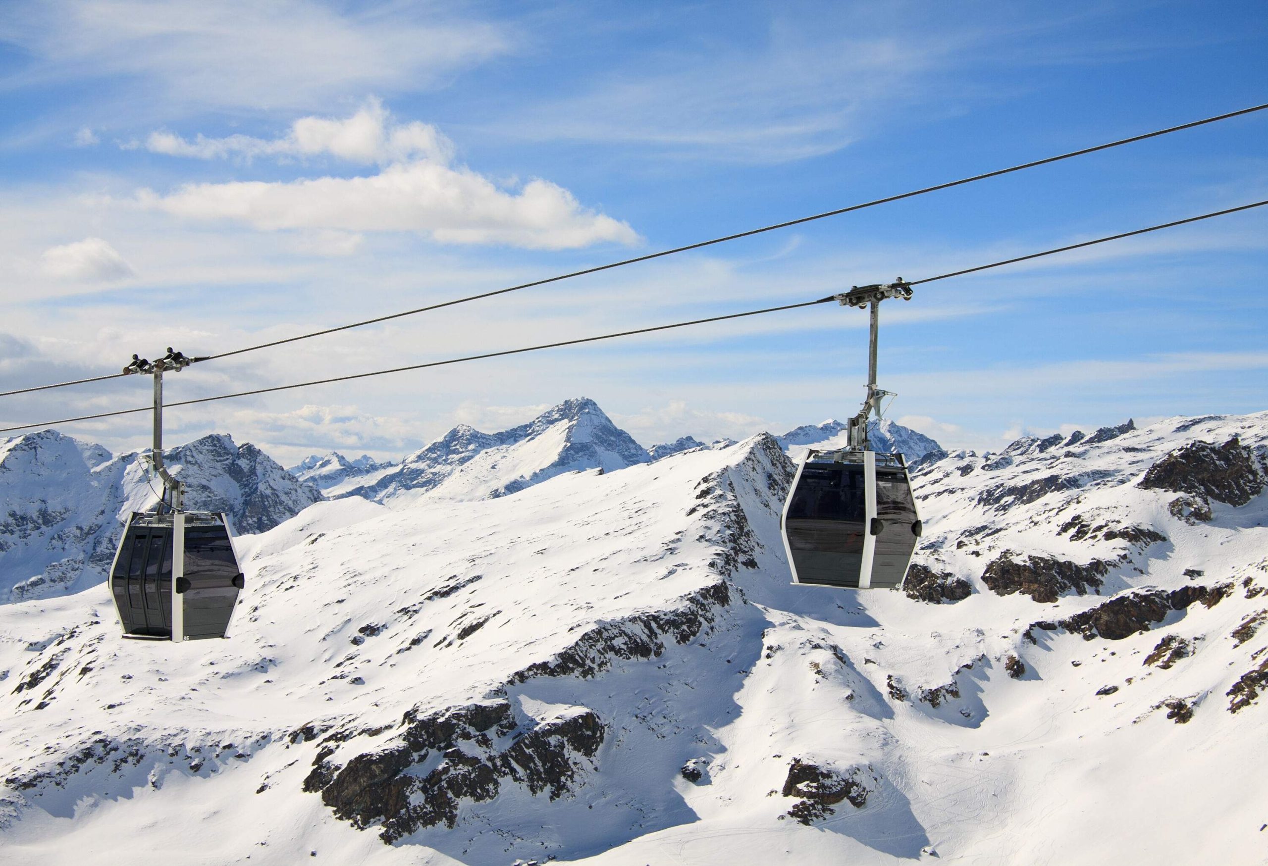 Two cable cars hover above a snow-covered terrain.