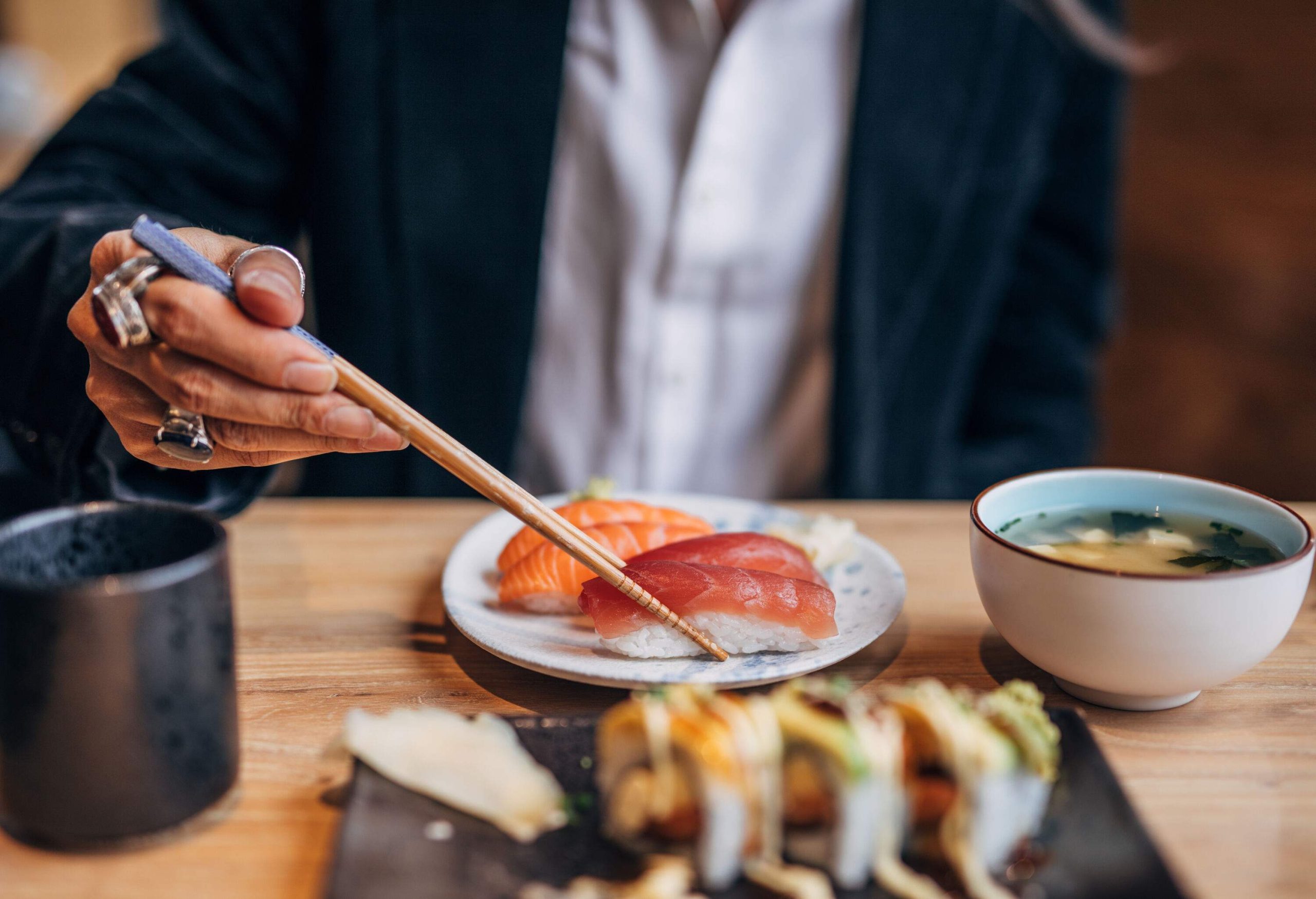 A hand picks a piece of sushi with chopsticks.