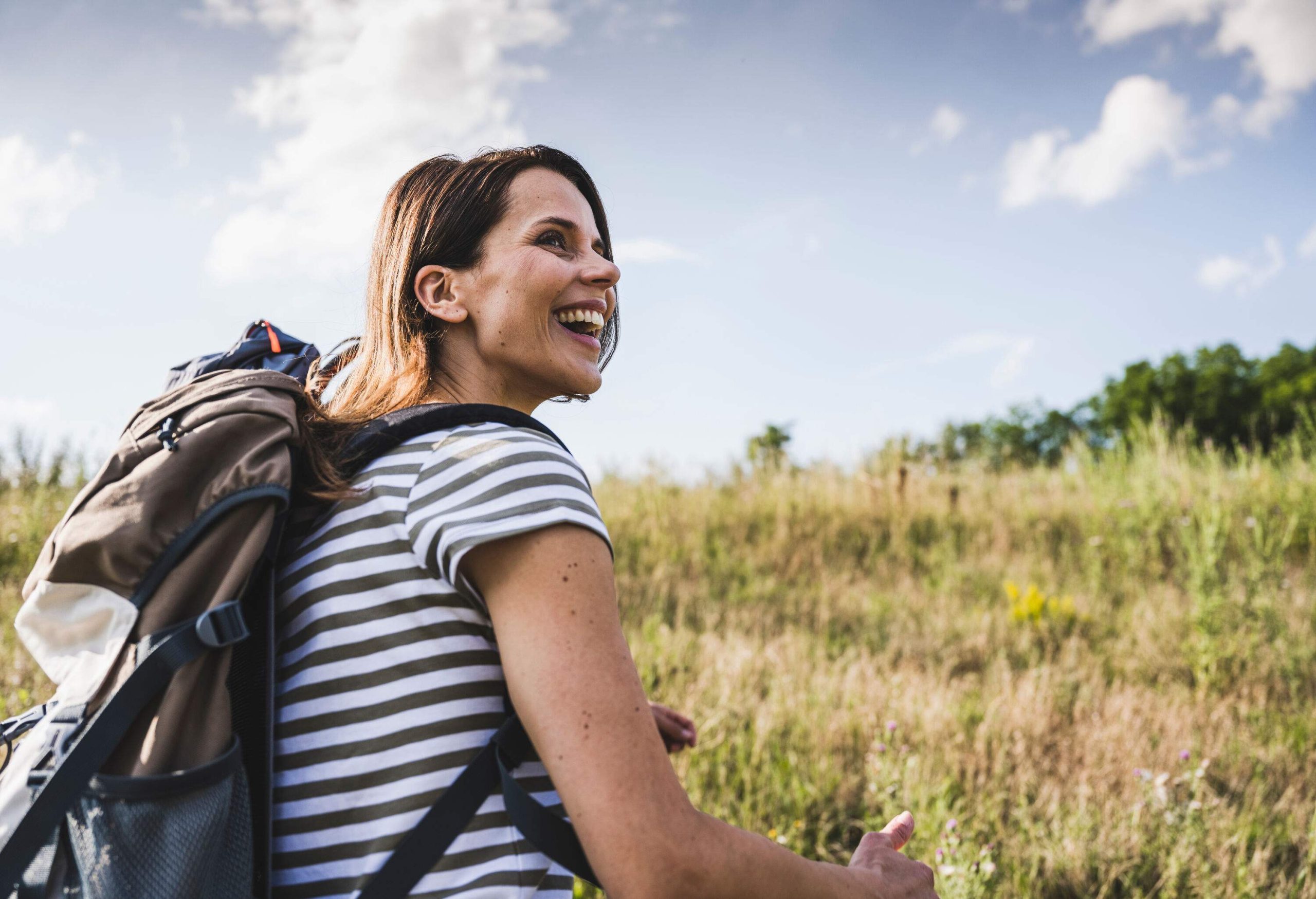 Woman with a striped shirt and bag laughs and looks behind her.