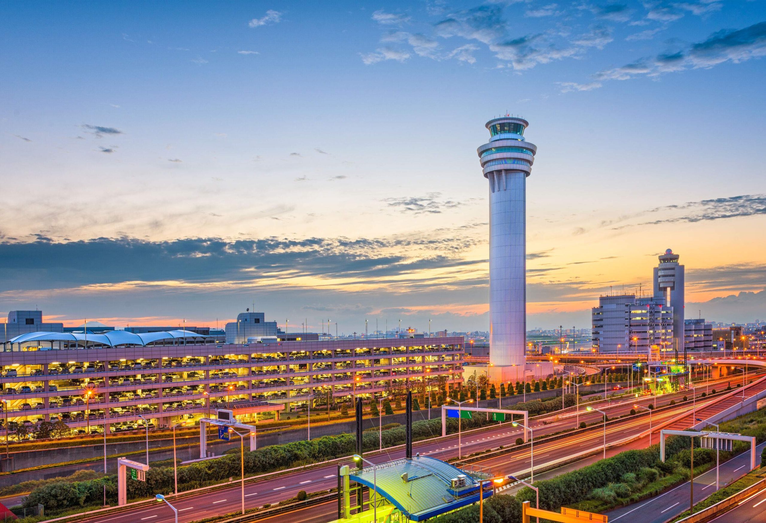 A tall white airport control tower protrudes toward the scenic sky dominating the buildings in the foreground.