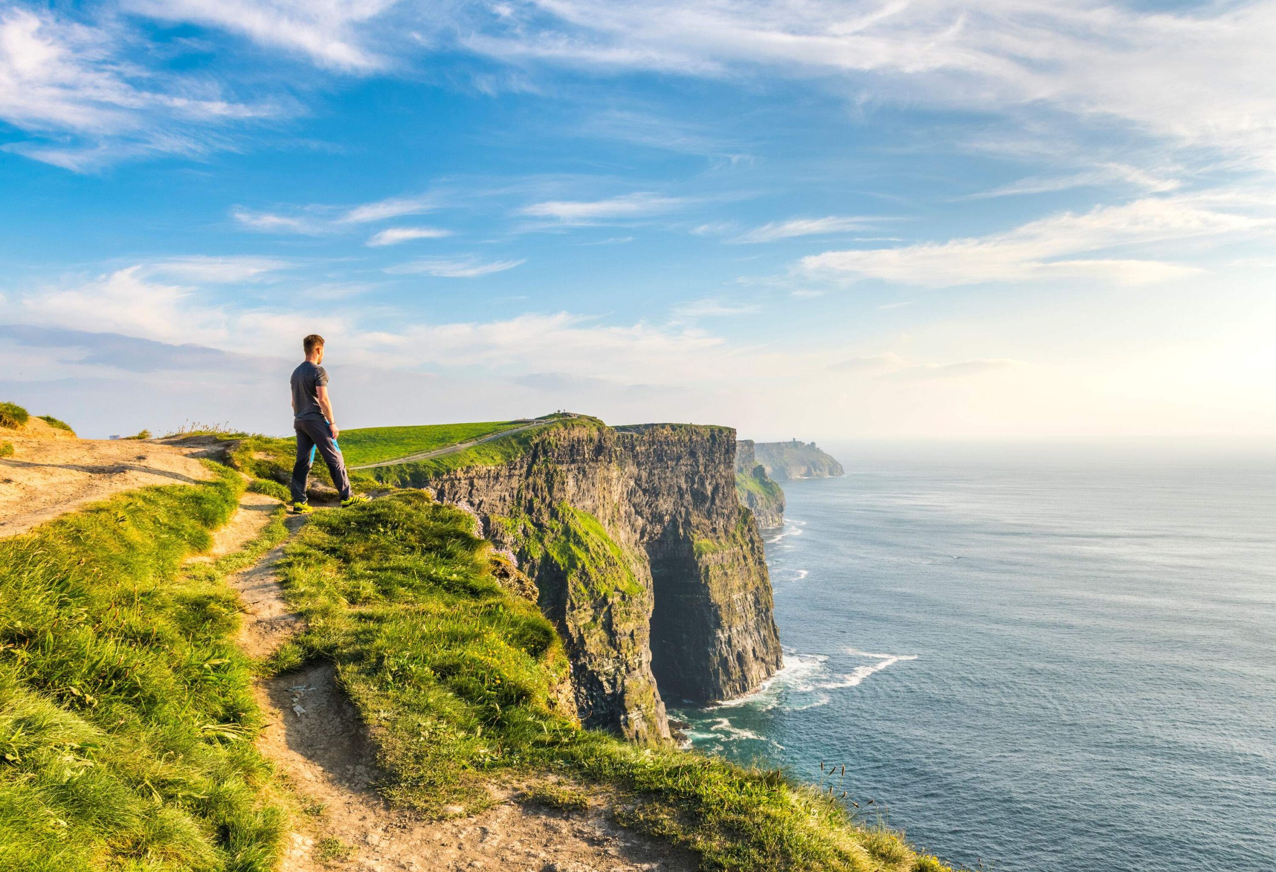 A man walking on a trail towards the edge of the Cliffs of Moher.