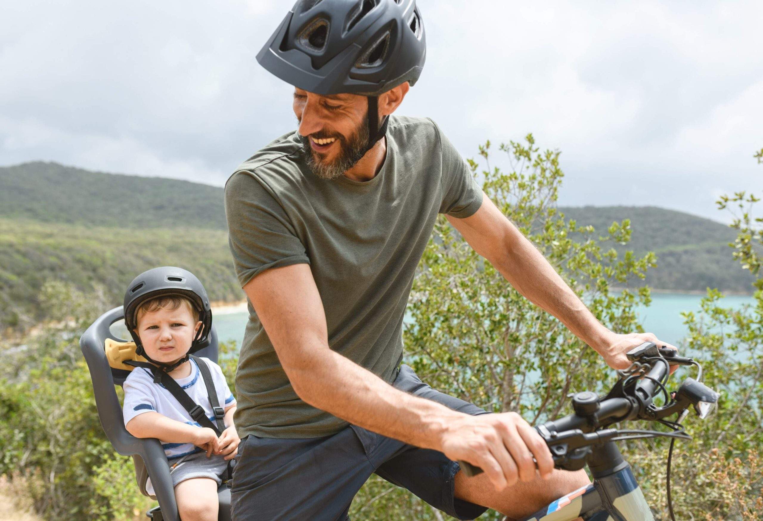 A man riding his bicycle with a young child in the backseat.