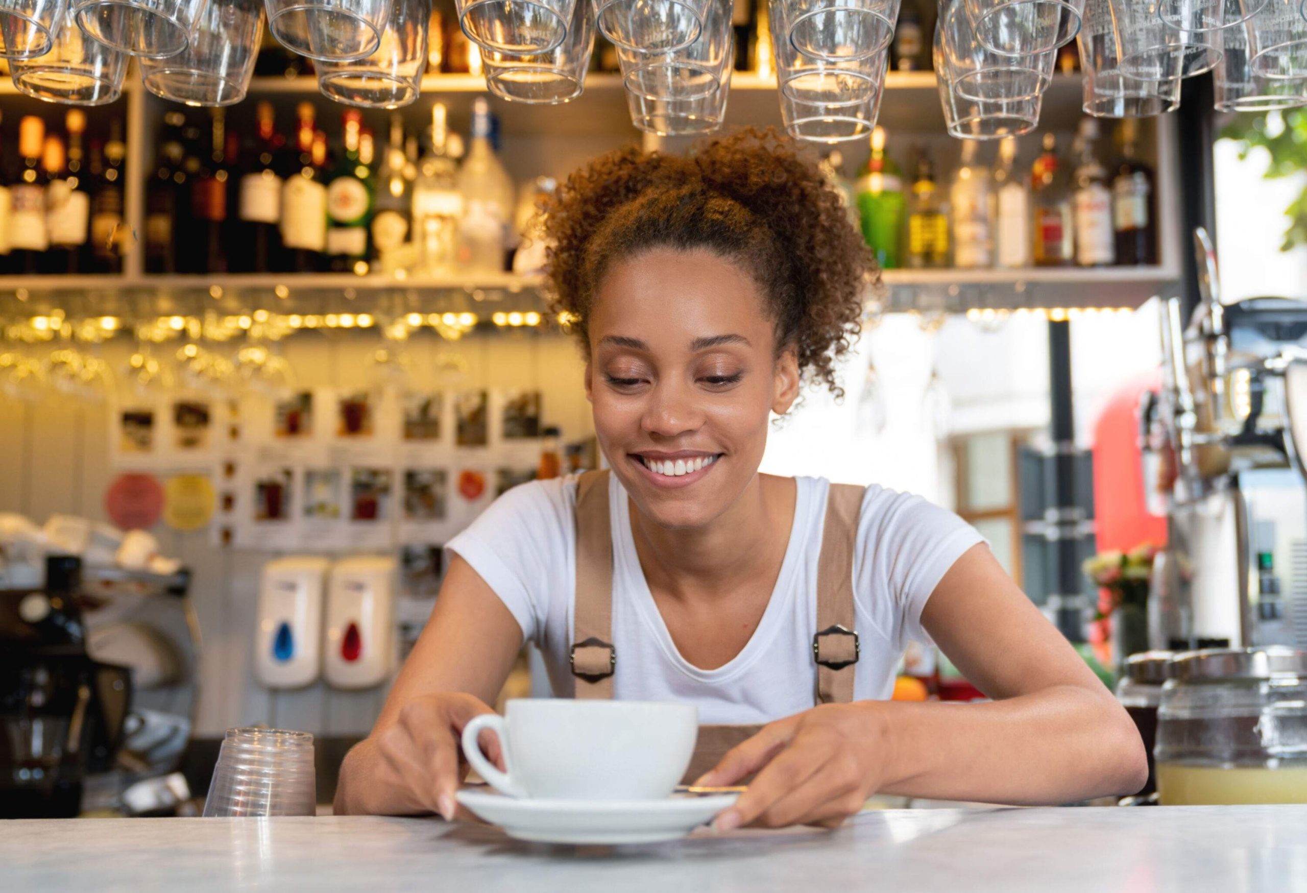 A woman behind the counter in a cafe holding a teacup and saucer.