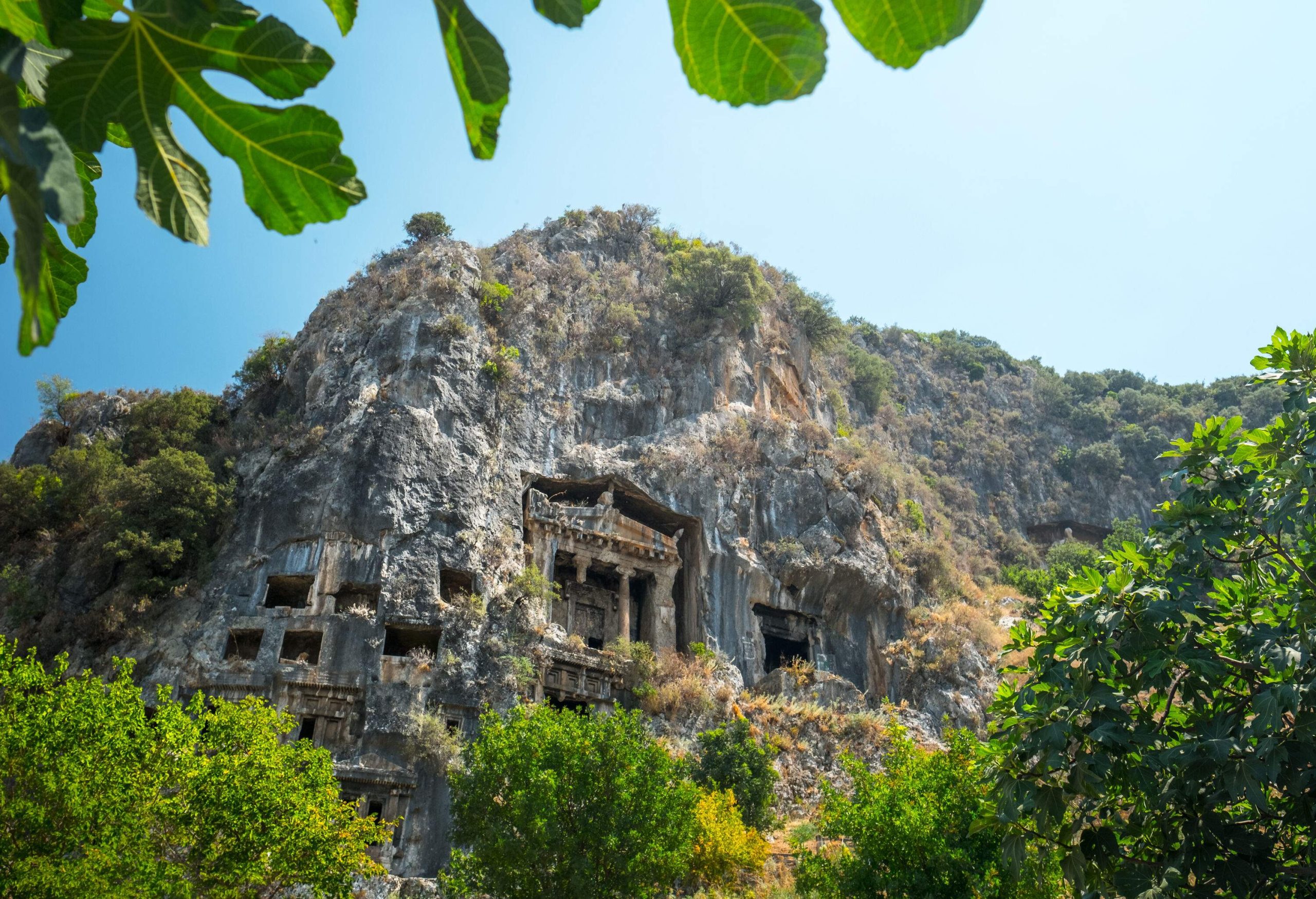 Historical rock tombs of pediments with columns are hewn from the lush cliff face.